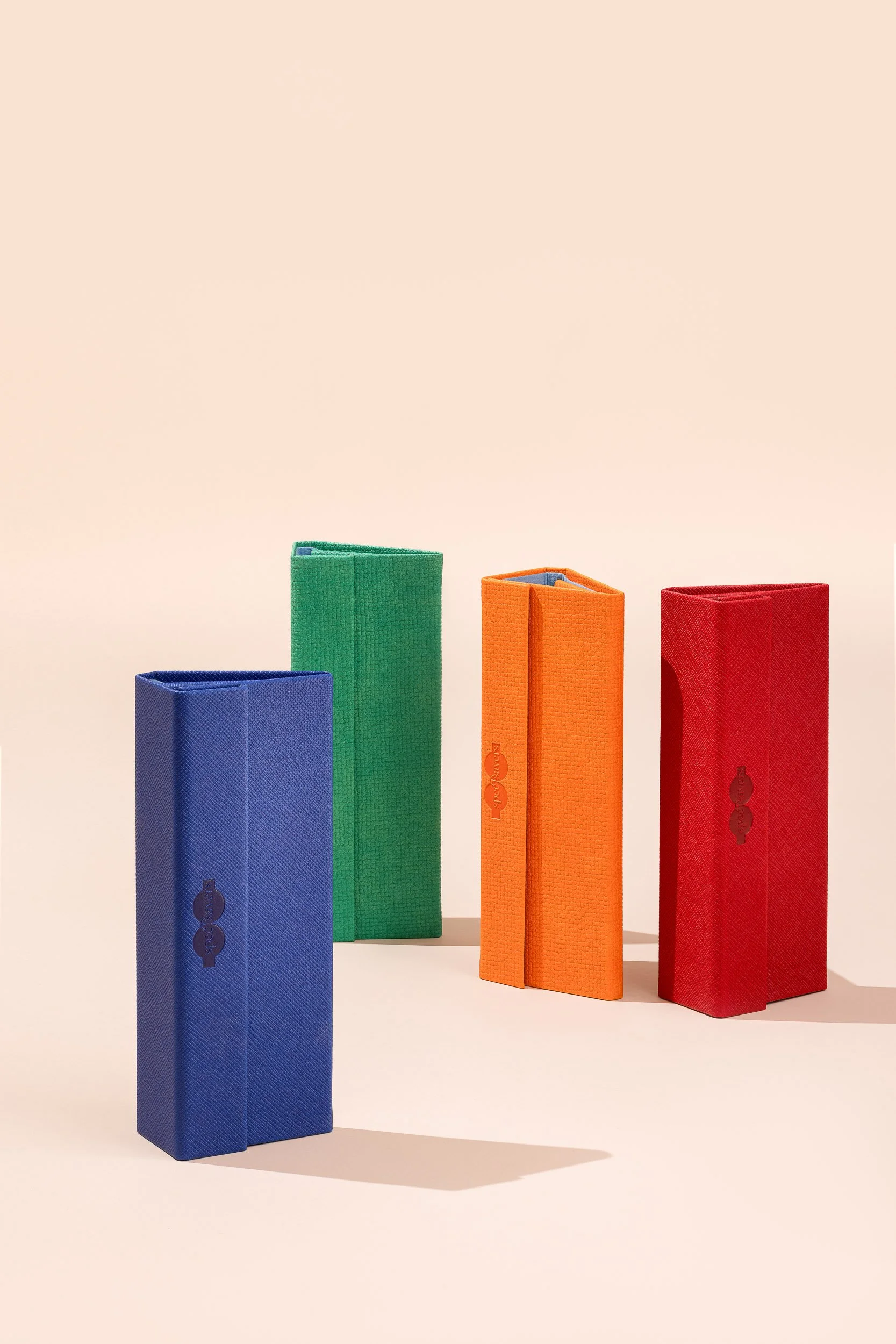 Five yoga blocks arranged in a row, from left to right: blue, green, orange, and red, on a light background.