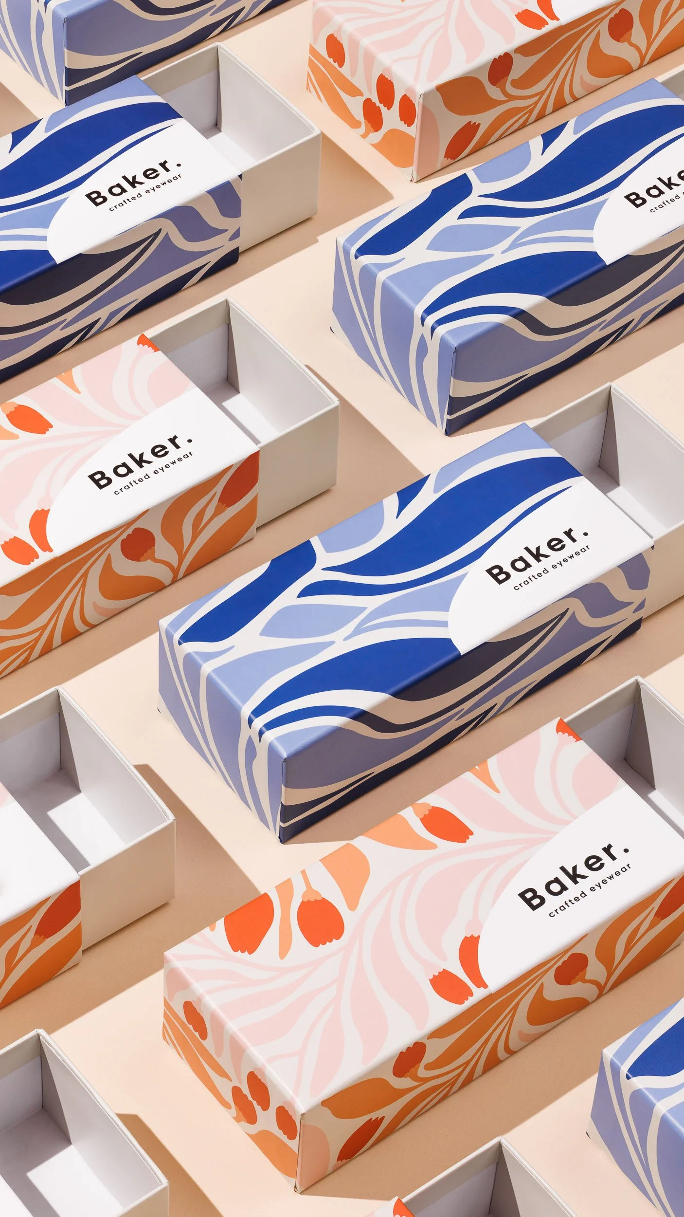Multiple boxes of eyewear packaging with blue and orange floral designs, labeled 'Baker crafted eyewear,' arranged on a light-colored surface.