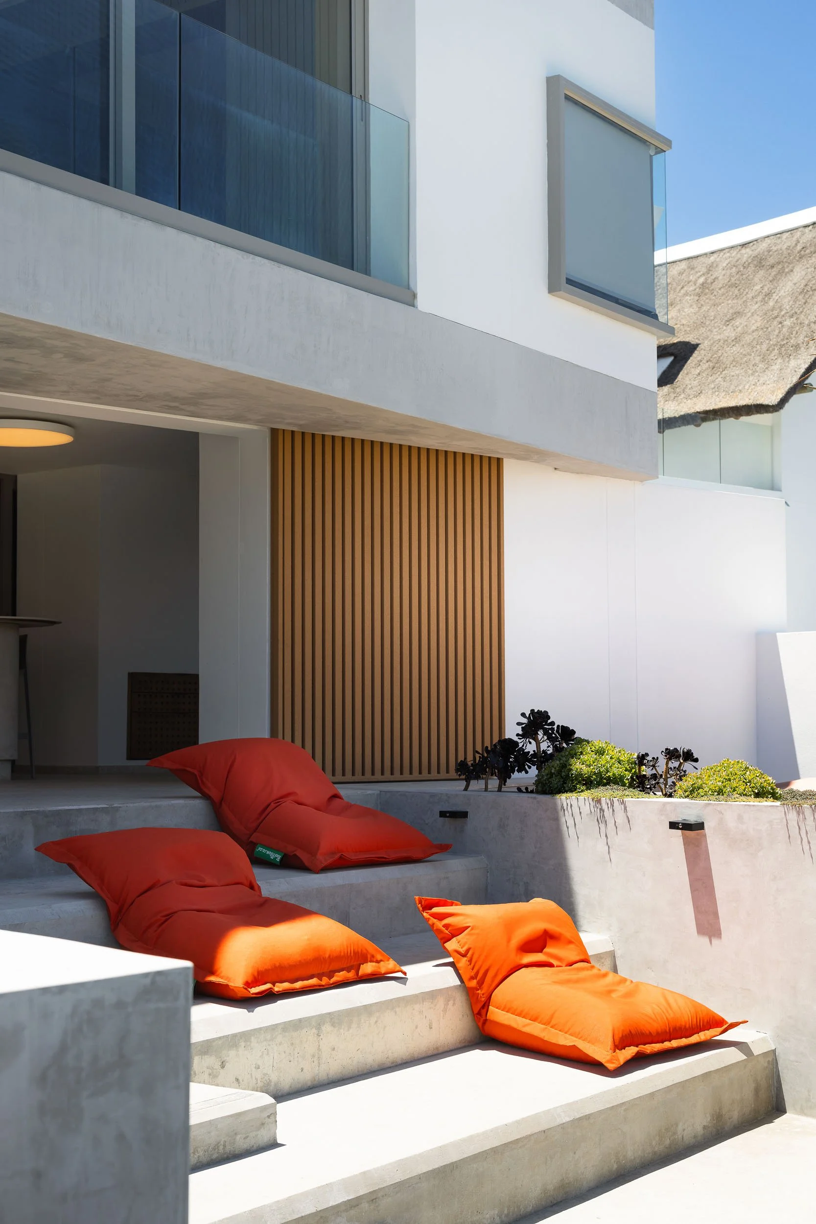 Cantilevered concrete terrace with orange bean bag cushions beside white rendered facade and timber screen