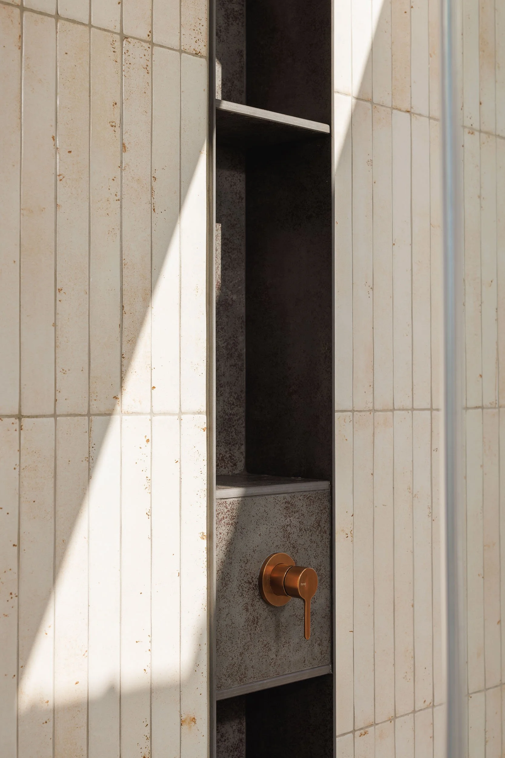 Shower niche detail with aged white elongated tiles, dark metal alcove, and brushed copper mixer