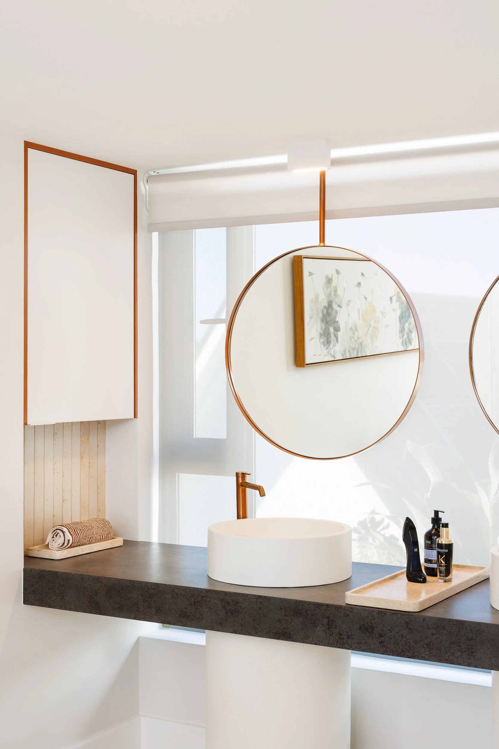Ensuite vanity with round copper-framed hanging mirrors, vessel basin, and dark stone bench top