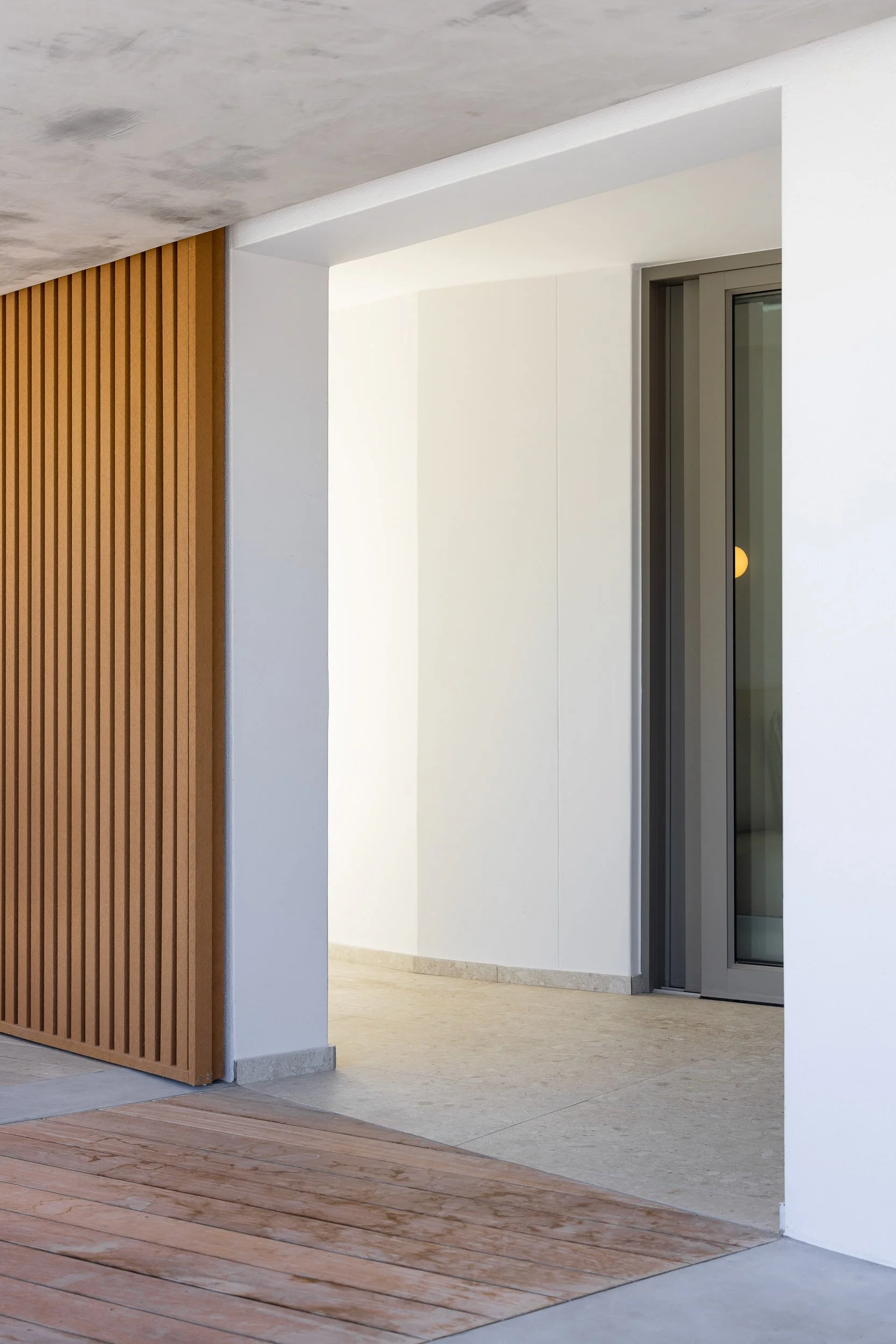 Covered entry threshold with warm timber batten screen, concrete soffit, and stone tile flooring