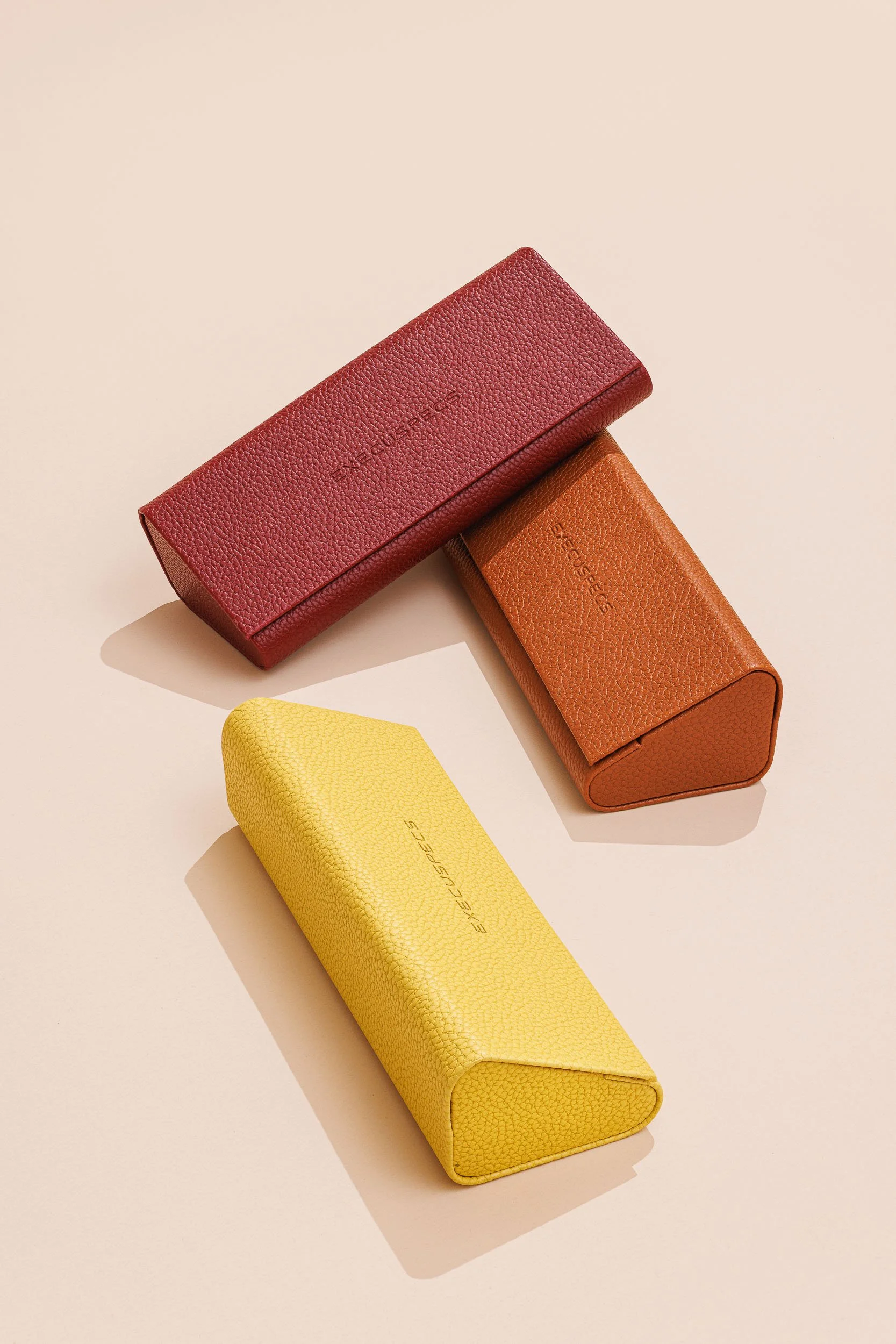 Three rectangular designer cases in red, orange, and yellow colors placed on a beige background.