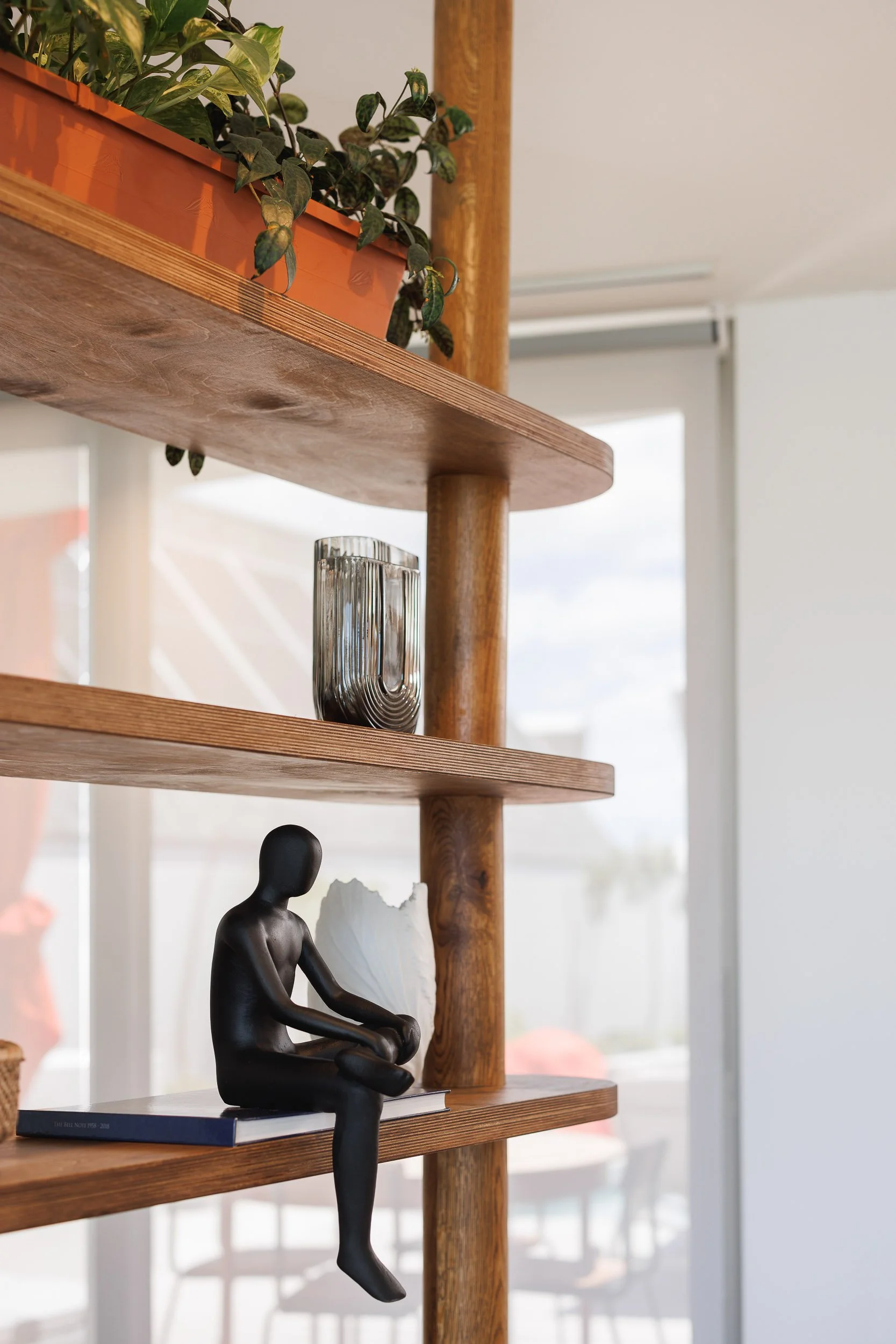 Close-up of timber freestanding shelving unit displaying black seated figurine and ribbed glass vase
