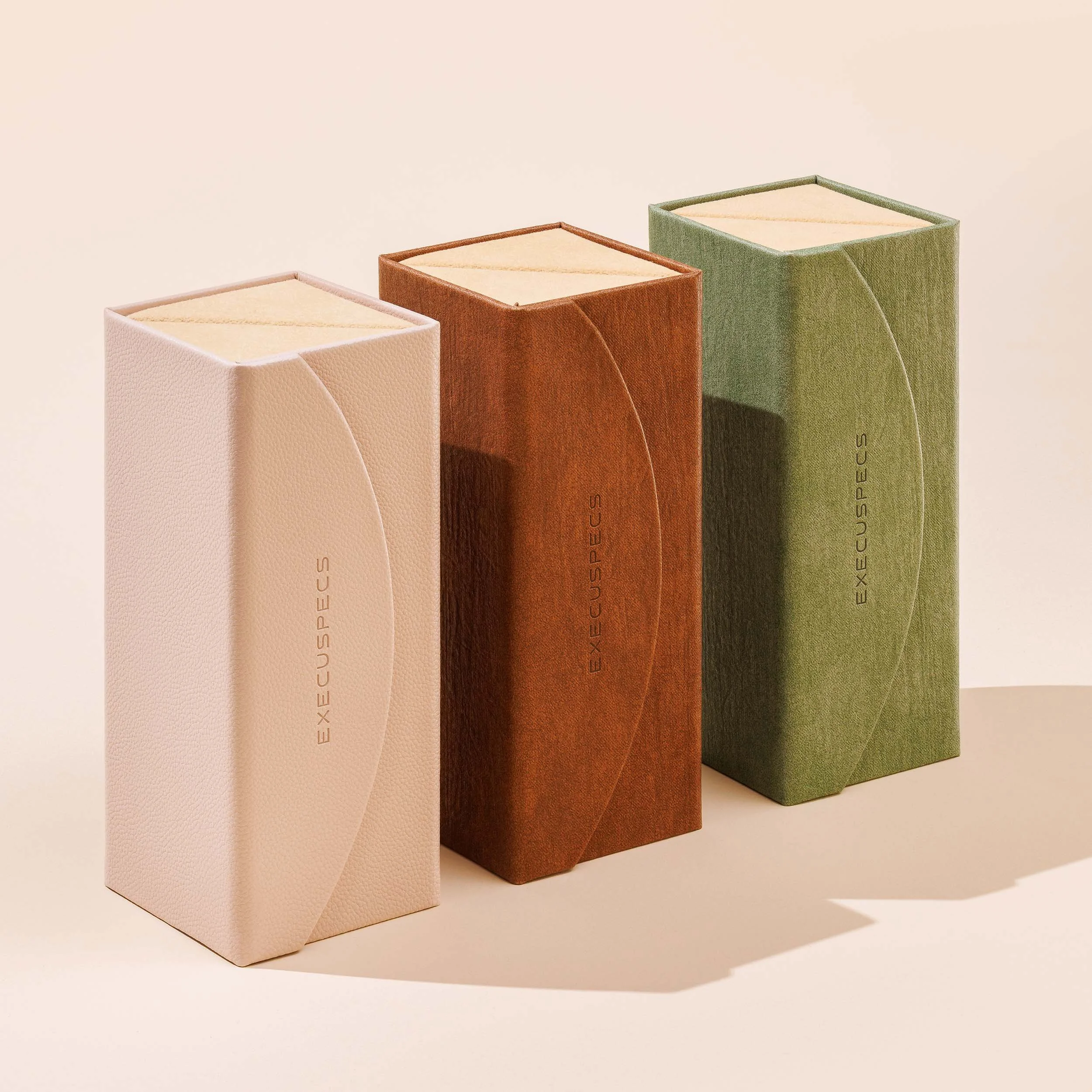 Three rectangular eyewear boxes in pastel colors pink, red, and green arranged in a row against a plain beige background.