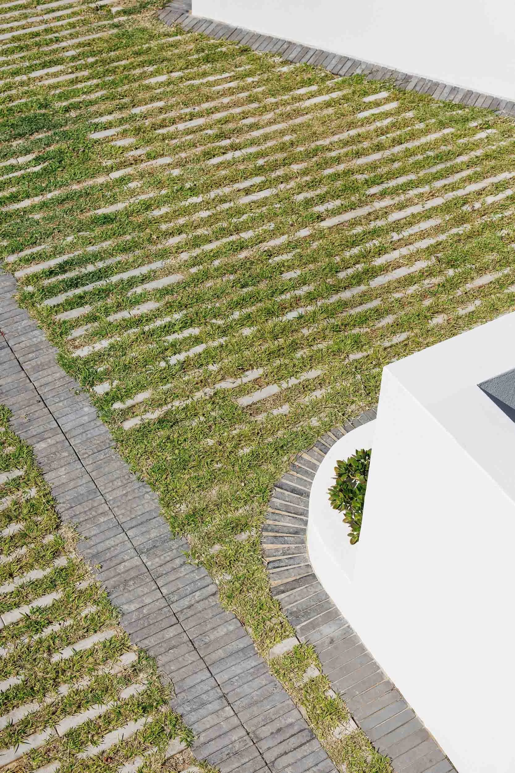 Overhead view of grass-jointed brick driveway paving with curved white rendered garden wall