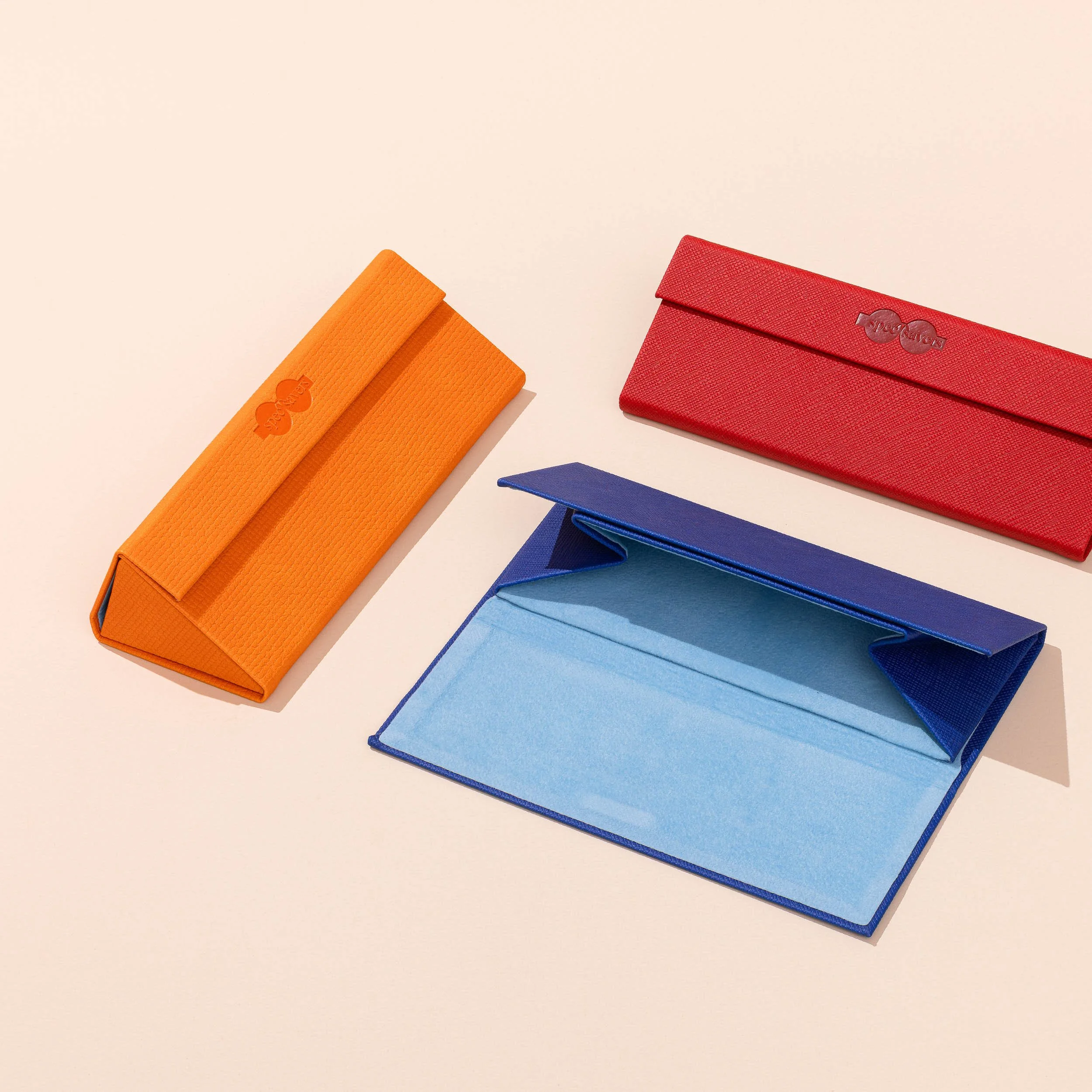 Various colorful wallets made of textured material, including orange, red, blue, and light blue, arranged on a light beige background.