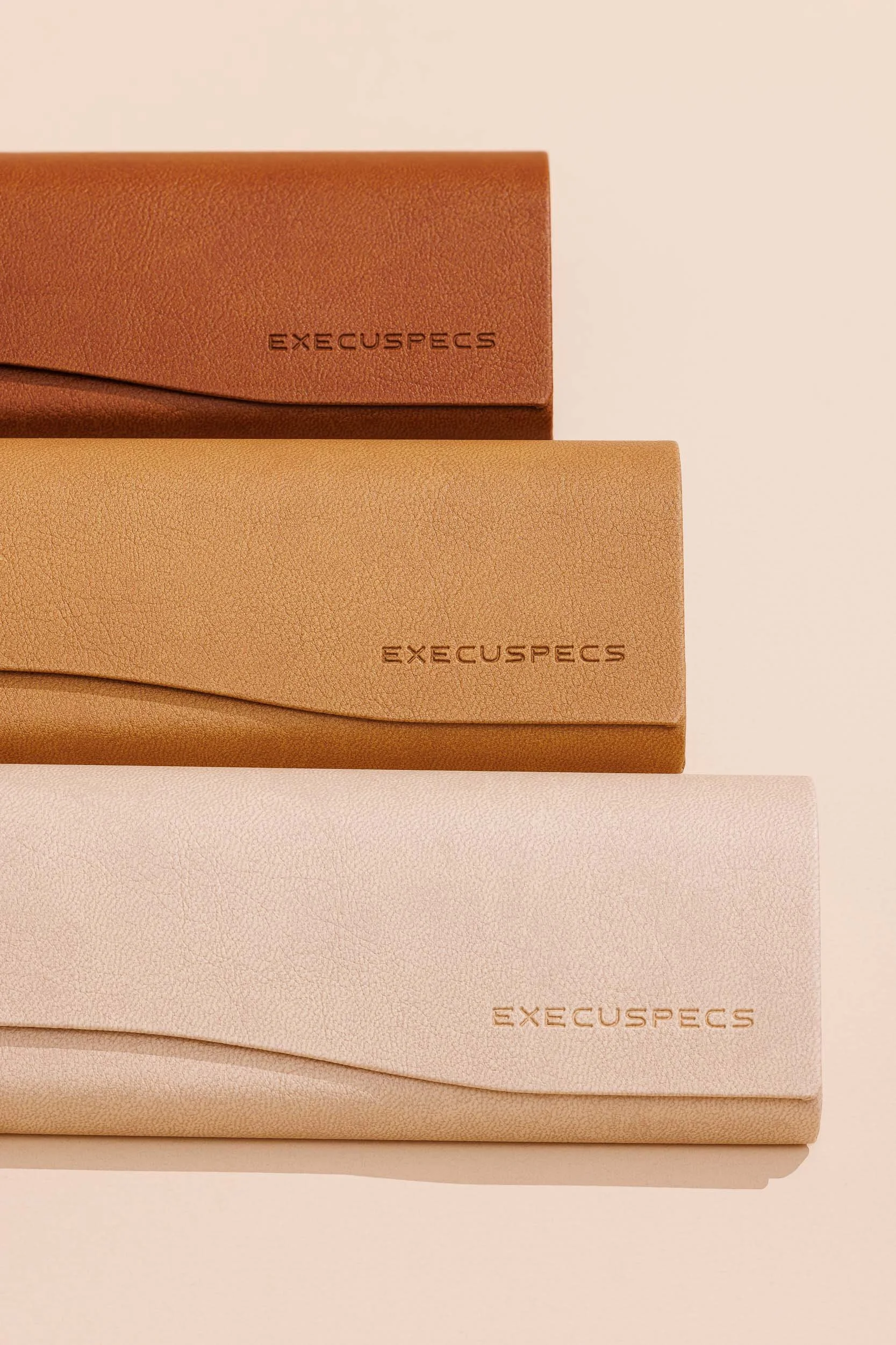 Three folded beige and tan leather straps with the brand name 'EXECUSEPCS' embossed on each.