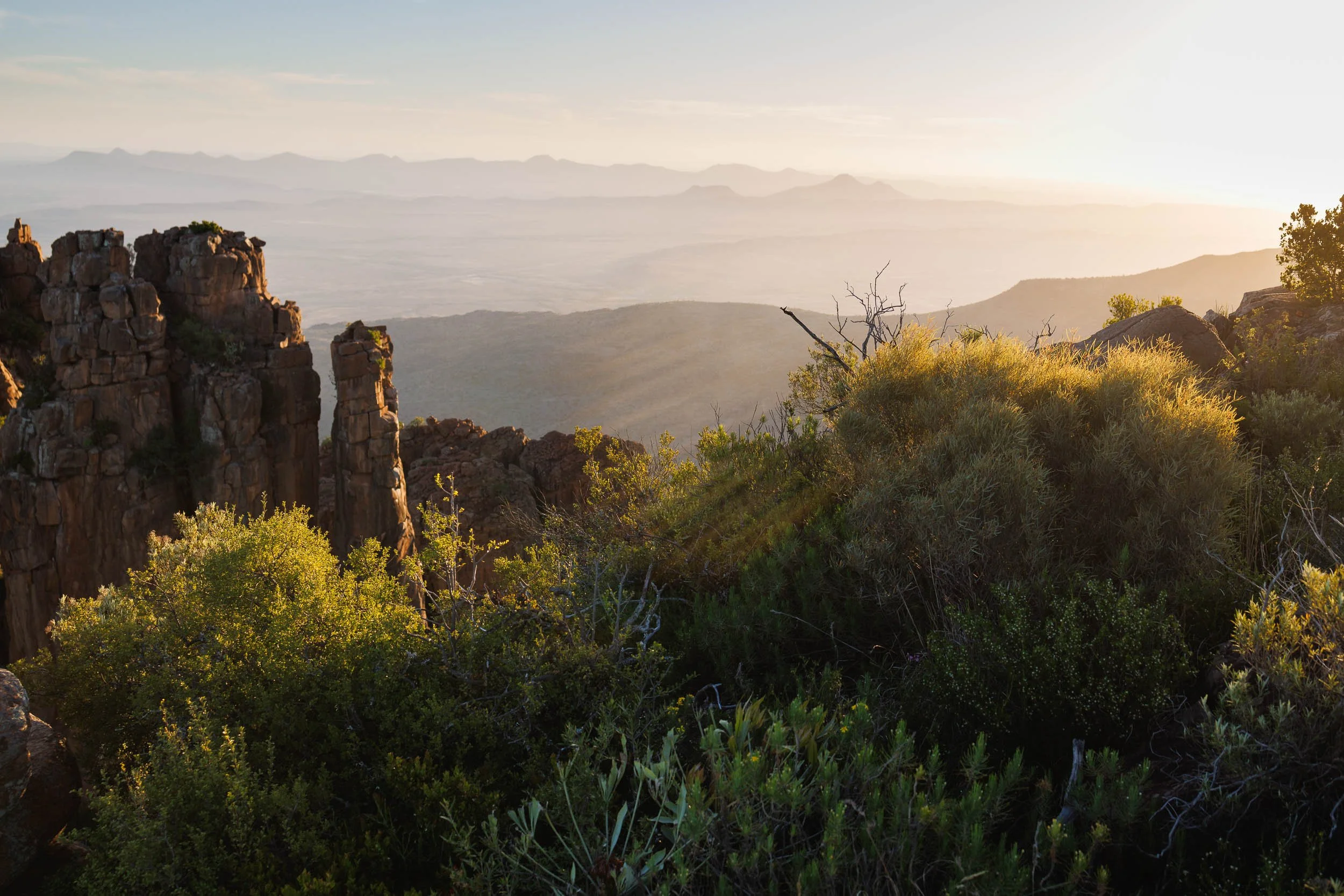 A scenic landscape of the Valley of Desolution showing rocky outcroppings, green shrubs, and distant mountains at sunset.