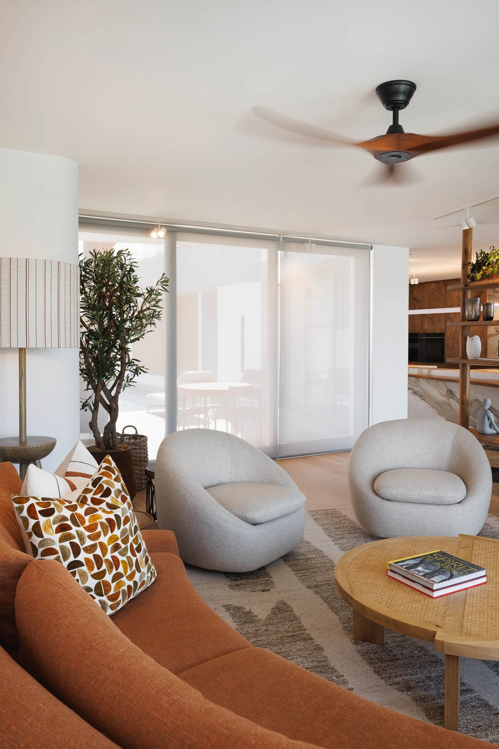 Living room with terracotta curved sofa, round grey swivel chairs, timber coffee table, and sheer panel blinds