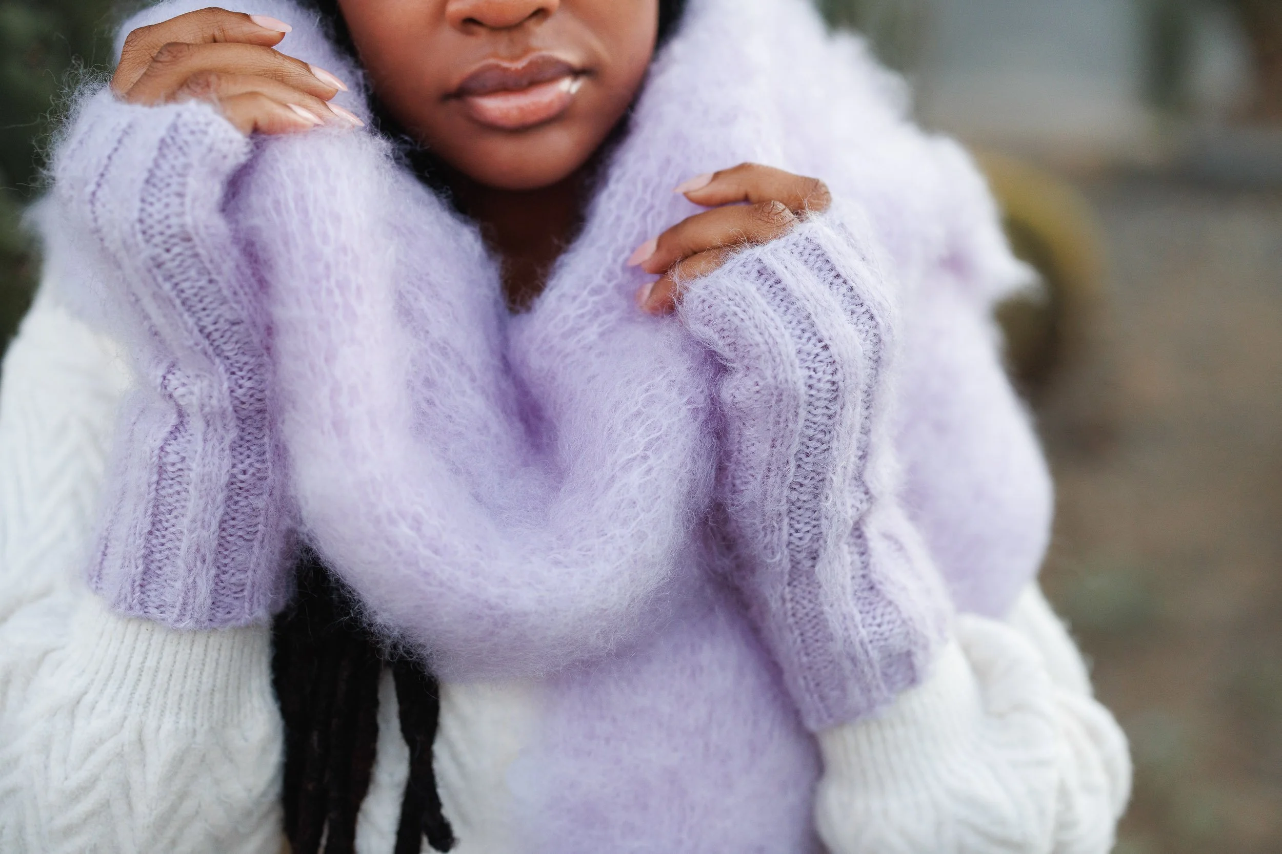 A woman wearing a fuzzy lavender sweater and off-white gloves, holding her head with both hands.