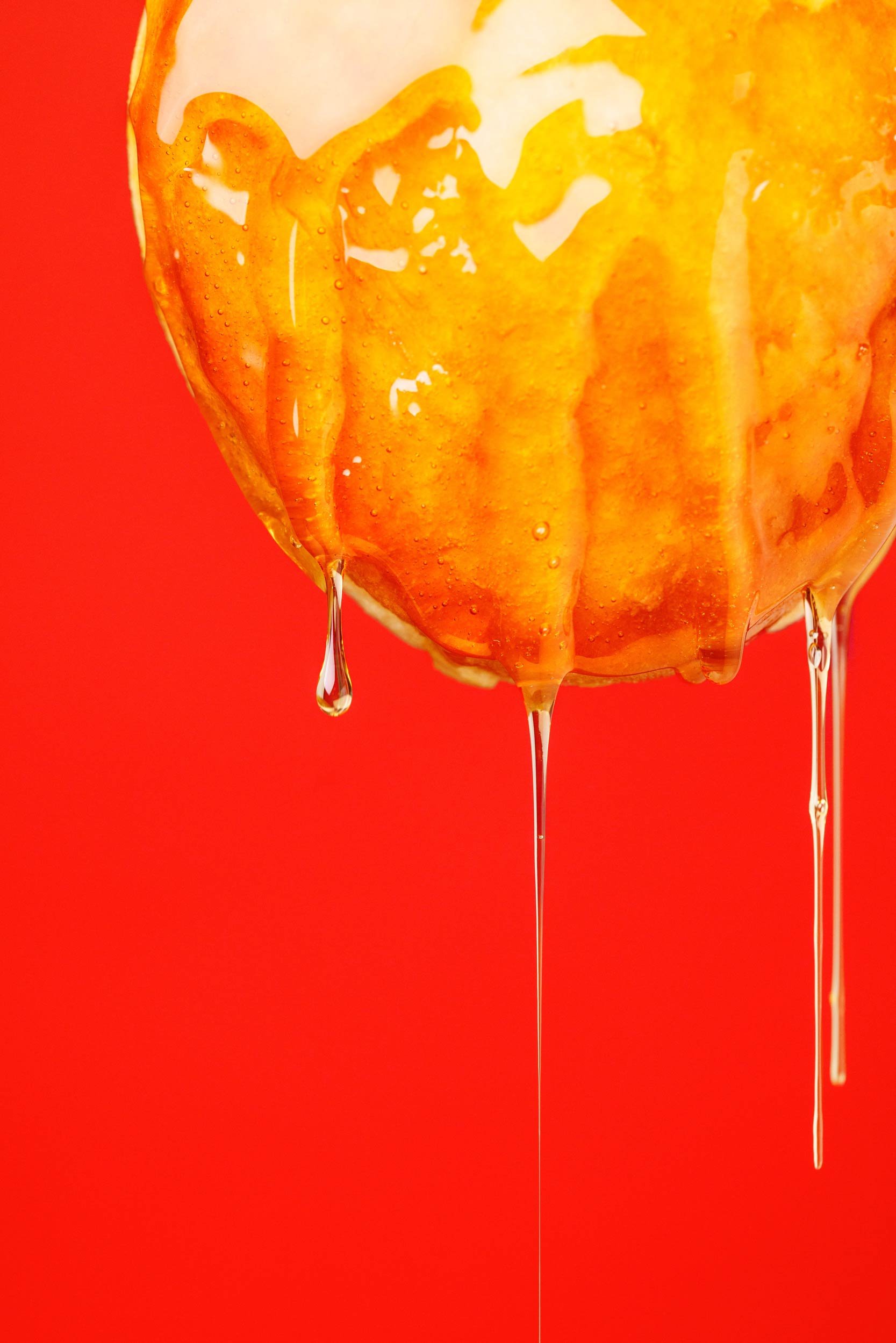Molten sugar dripping off the bottom of a glazed donut against a red background