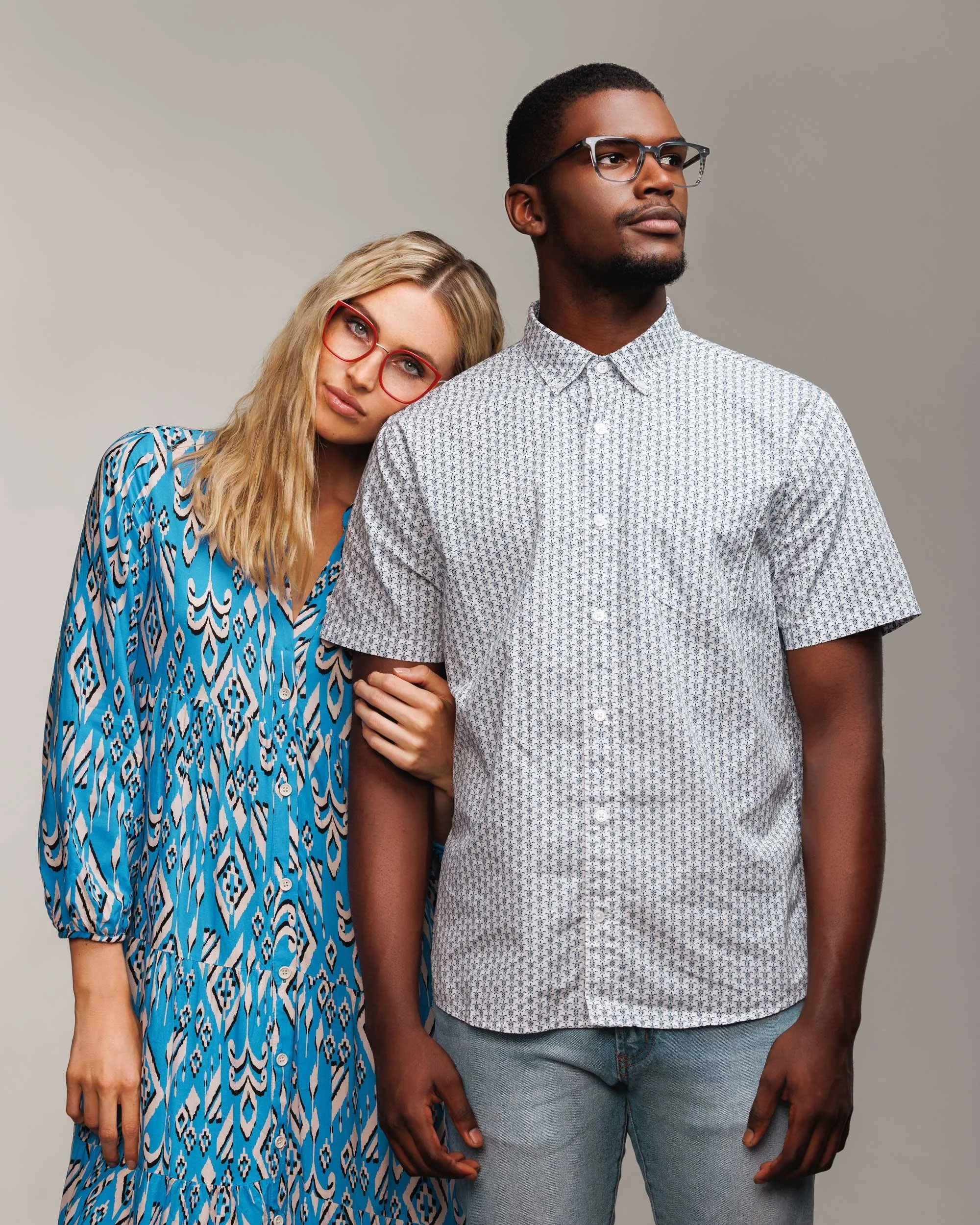 A blond woman wearing red glasses rest her head on the shoulder of a tall african man in a textured shirt