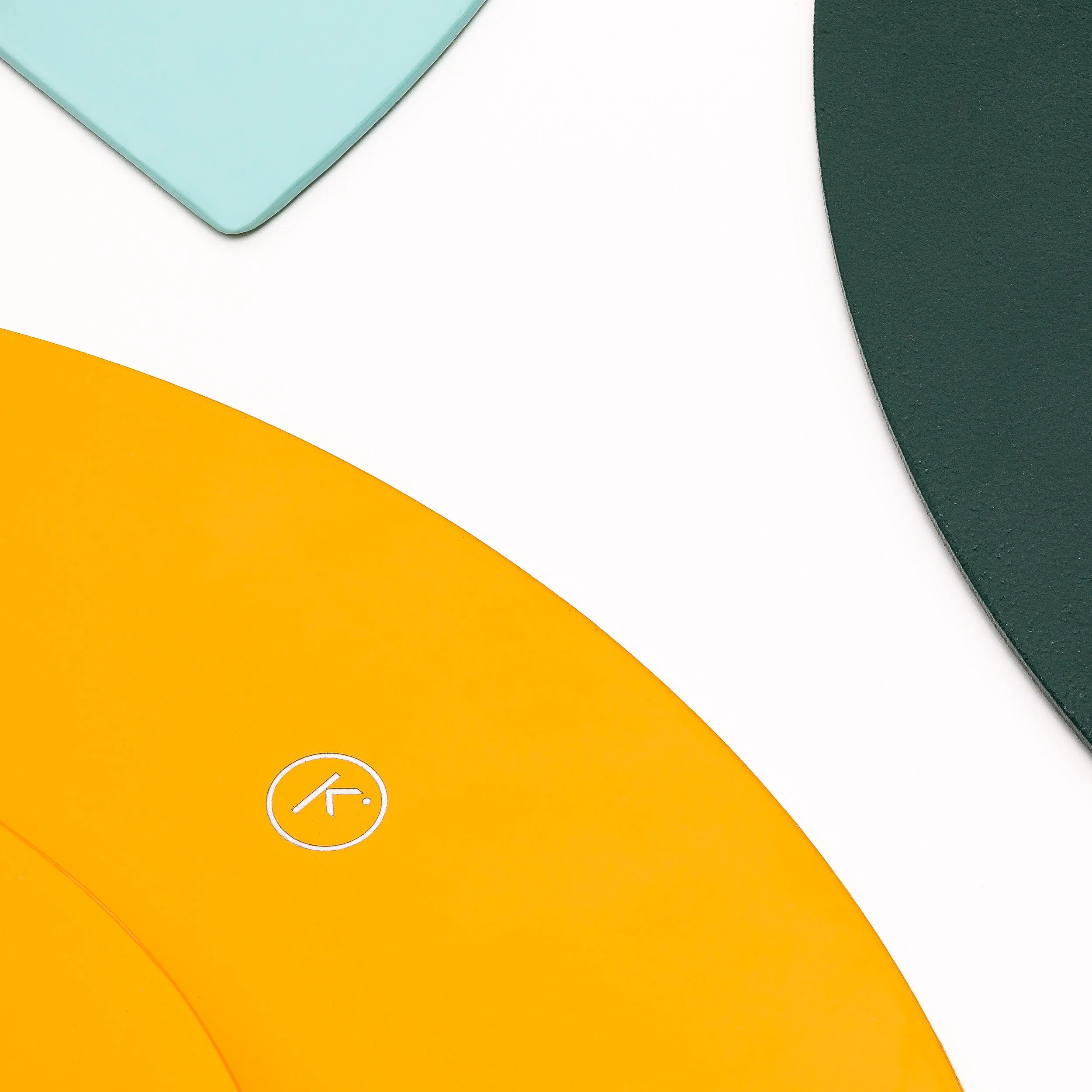 Close-up of a colorful geometric background with overlapping paper or fabric in green, white, yellow, and light blue colors. There is a small icon of a coffee cup with a slash through it on the yellow section.