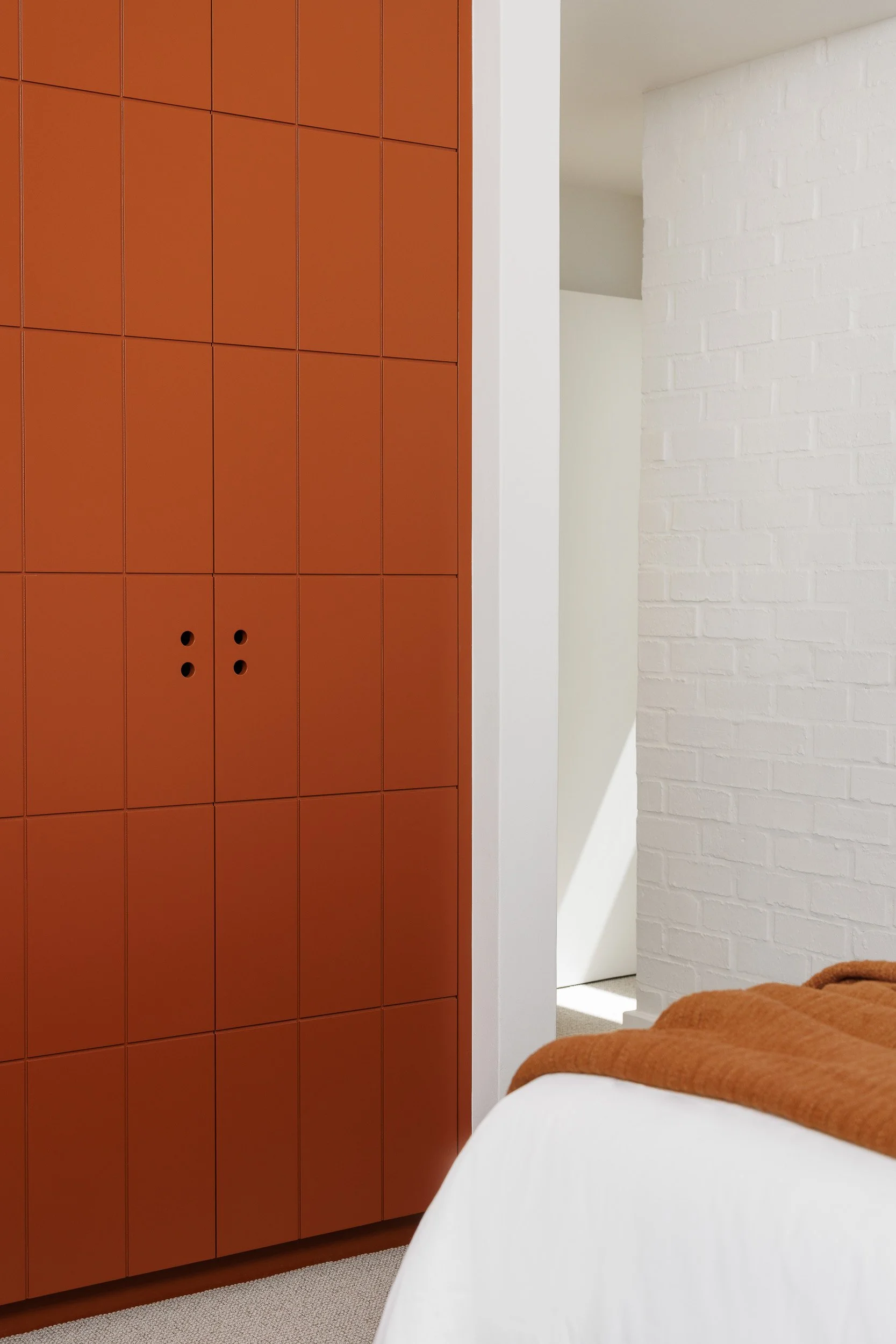Floor-to-ceiling terracotta panel cabinetry with dot-pull handles beside white painted brick bedroom wall
