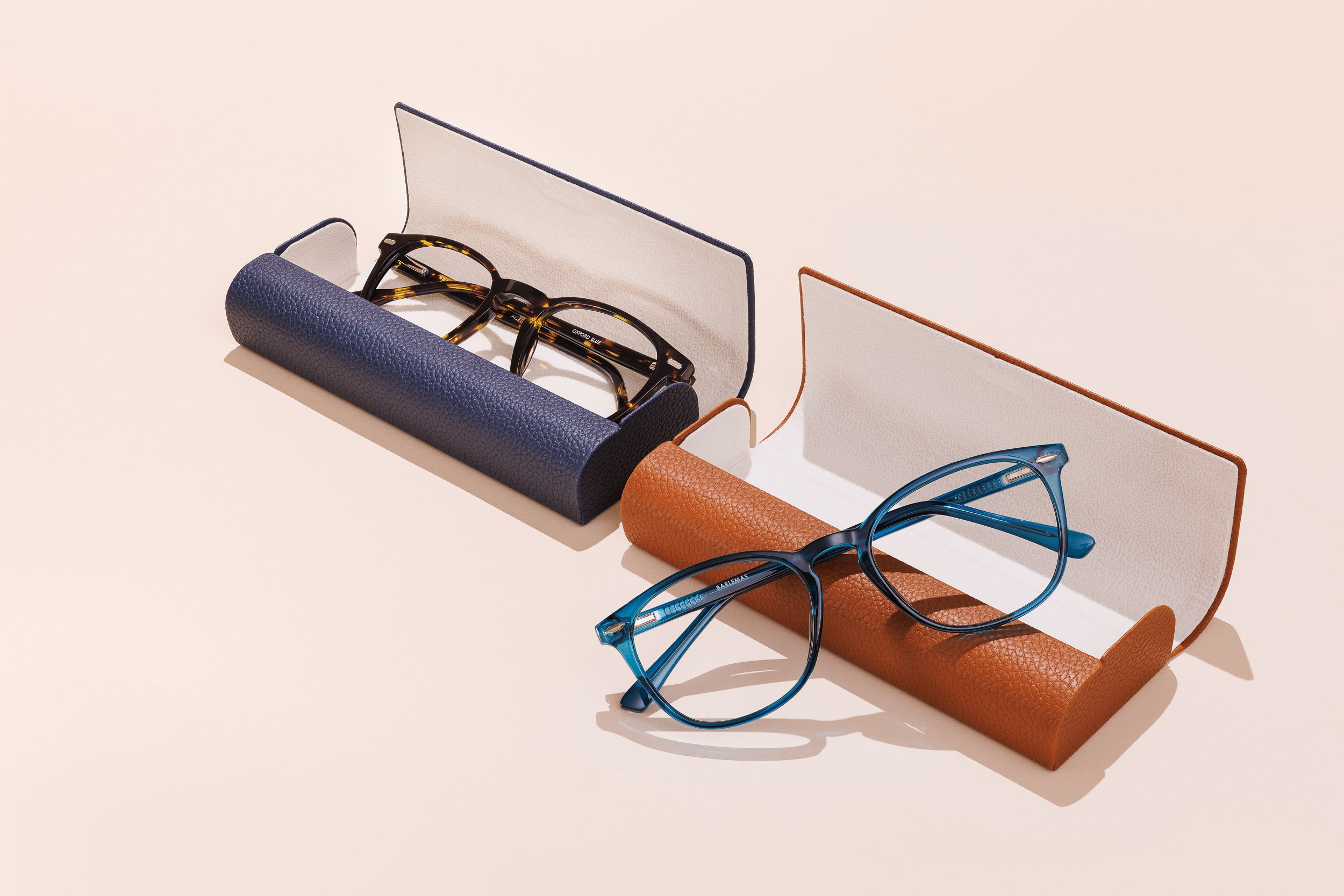 Three pairs of eyeglasses resting in cases, with two cases upright and open, arranged on a light background.