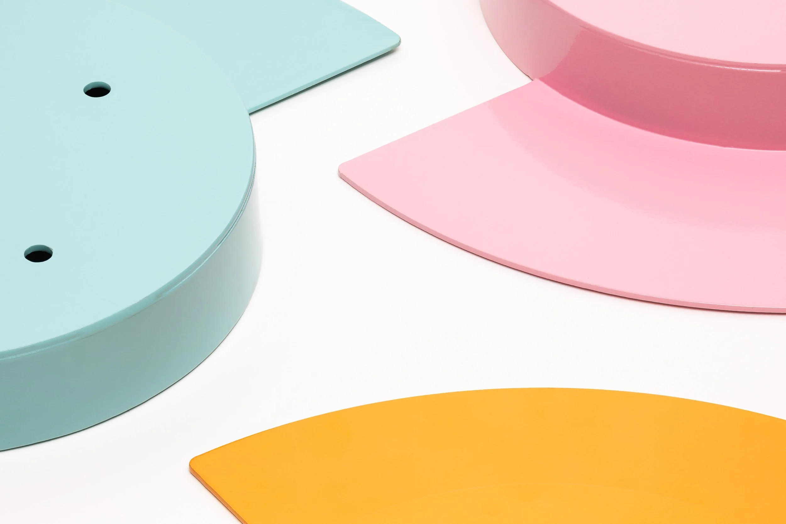 Close-up of colorful rounded objects in pastel colors, including blue, pink, orange, and green, on a white background.