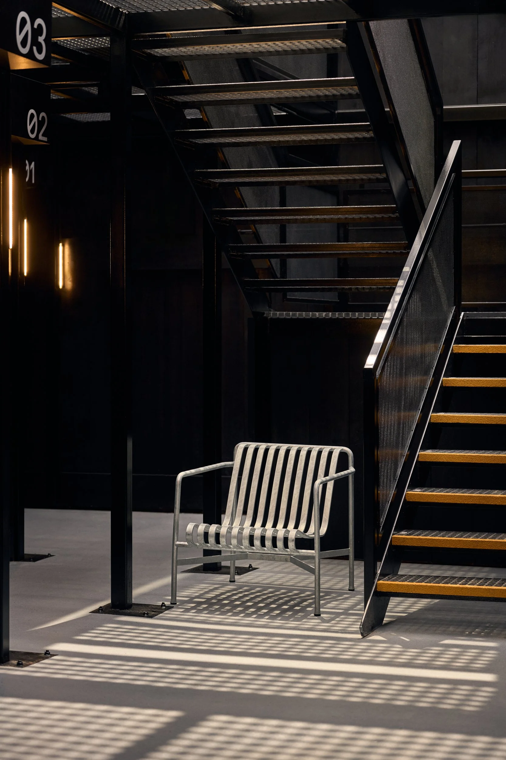 Empty modern metal bench in a black interior space with staircase casting striped shadows on the floor.