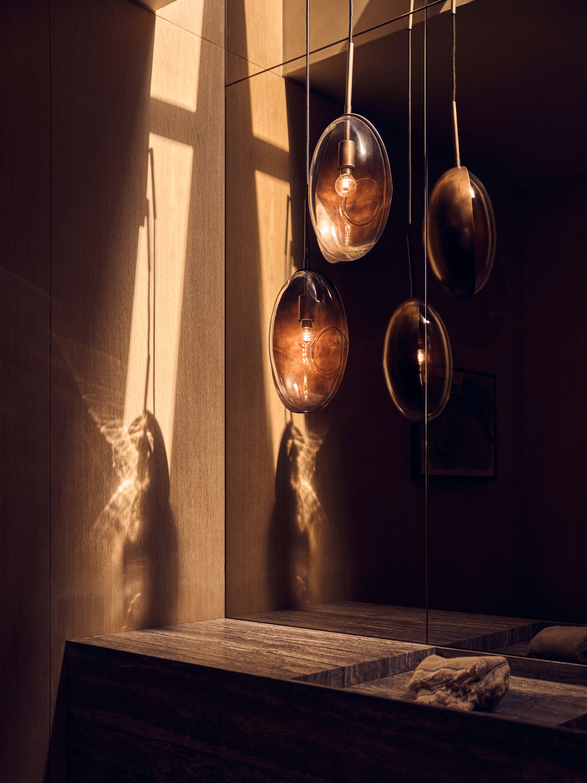 Modern display with hanging metallic lamps casting warm light and shadows on wood-paneled wall