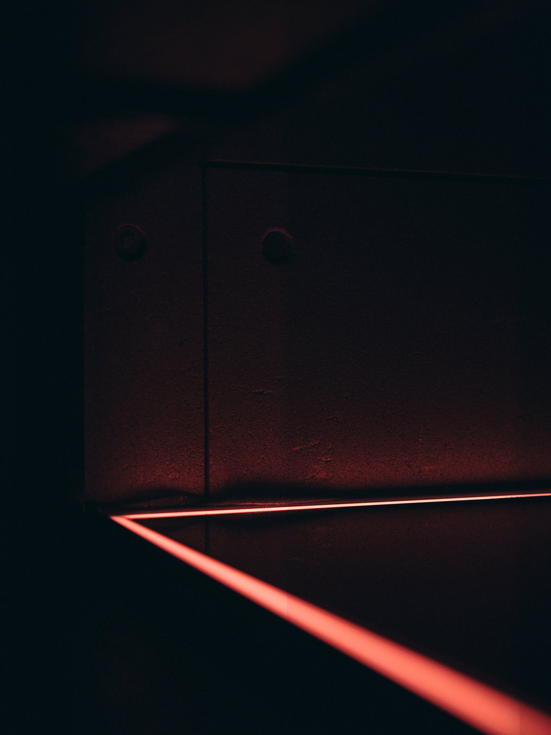 Dark room with a red neon light strip on the floor and a faint red glow at the top, with a vertical line in the center of the image.