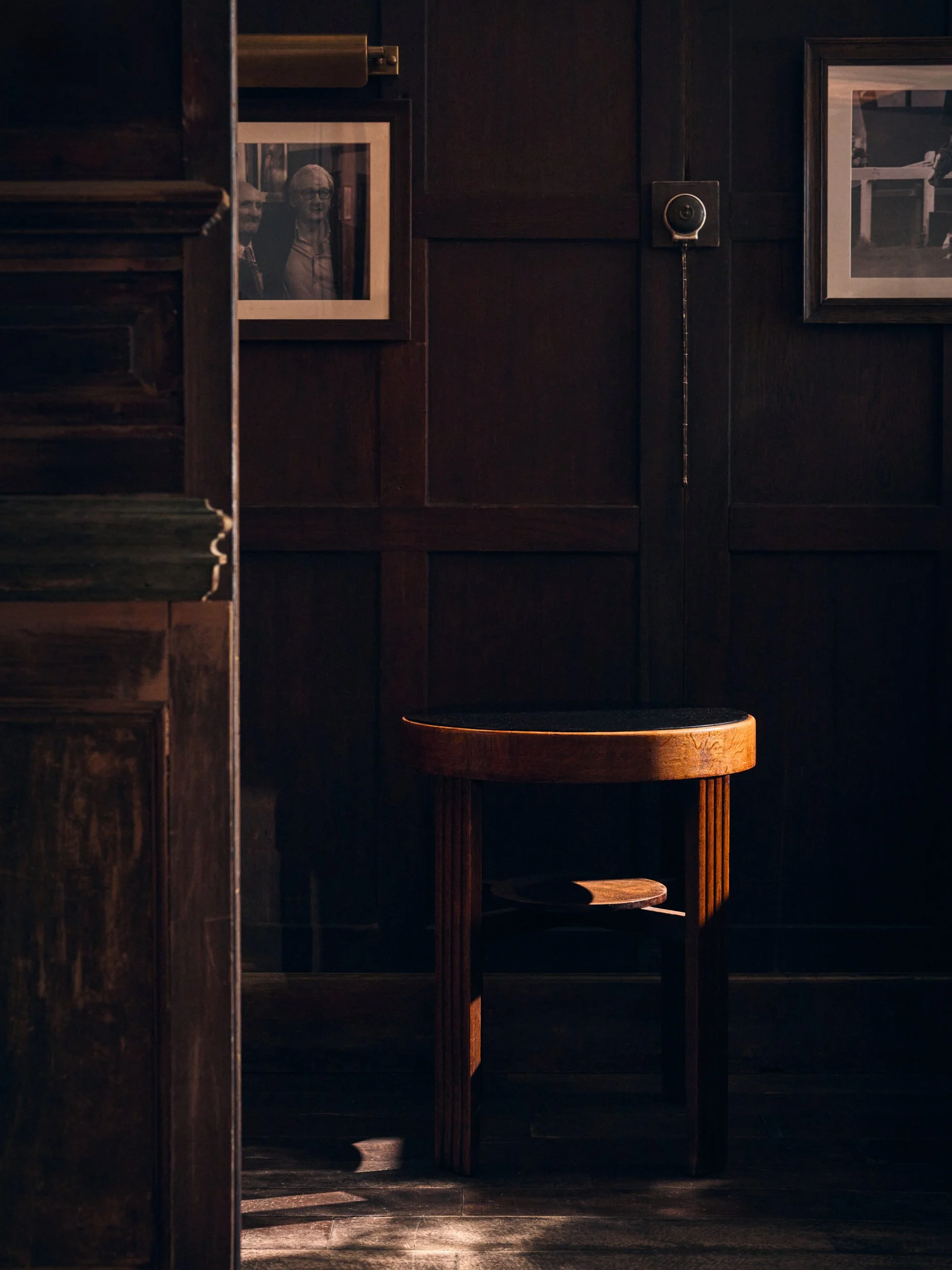 A dark wooden interior with framed photographs on the wall and a wooden stand in the corner. Sample lighting casts shadows and reflections.