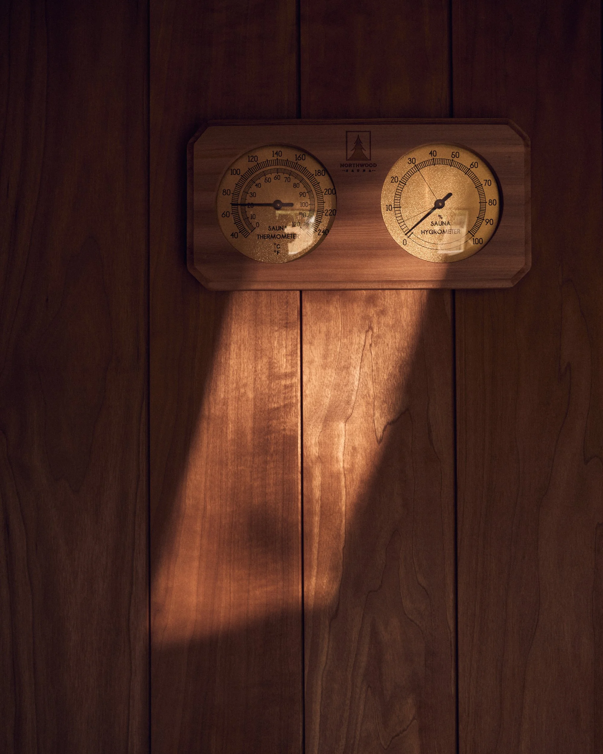 A wooden wall clock with two circular dials, one displaying temperature in Celsius and Fahrenheit and the other showing humidity percentage, both branded with Northwood label and a pine tree logo.