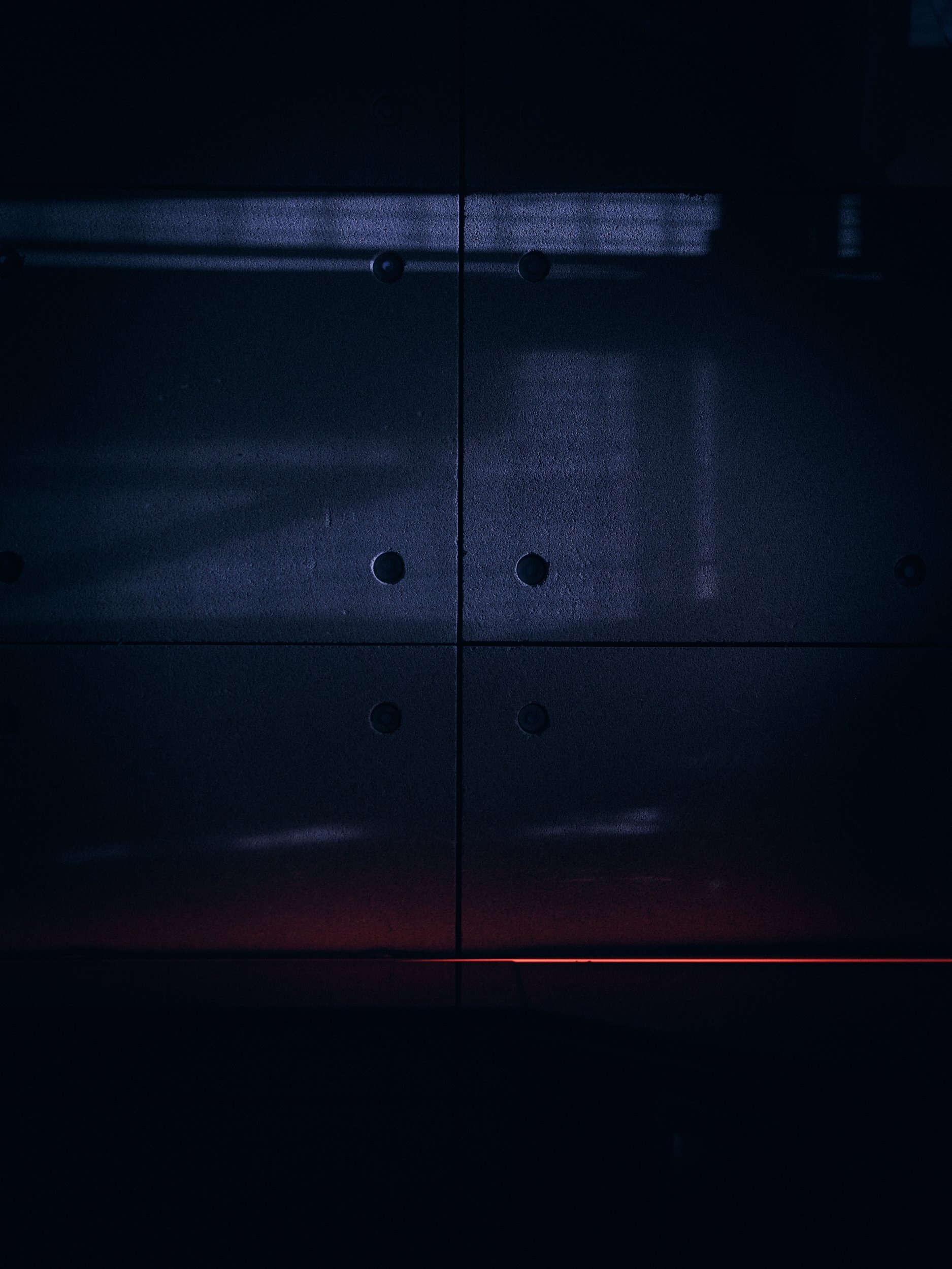 Dark metallic surface with a horizontal illuminated strip of light and small round screw holes, possibly part of a machine or electronic device.