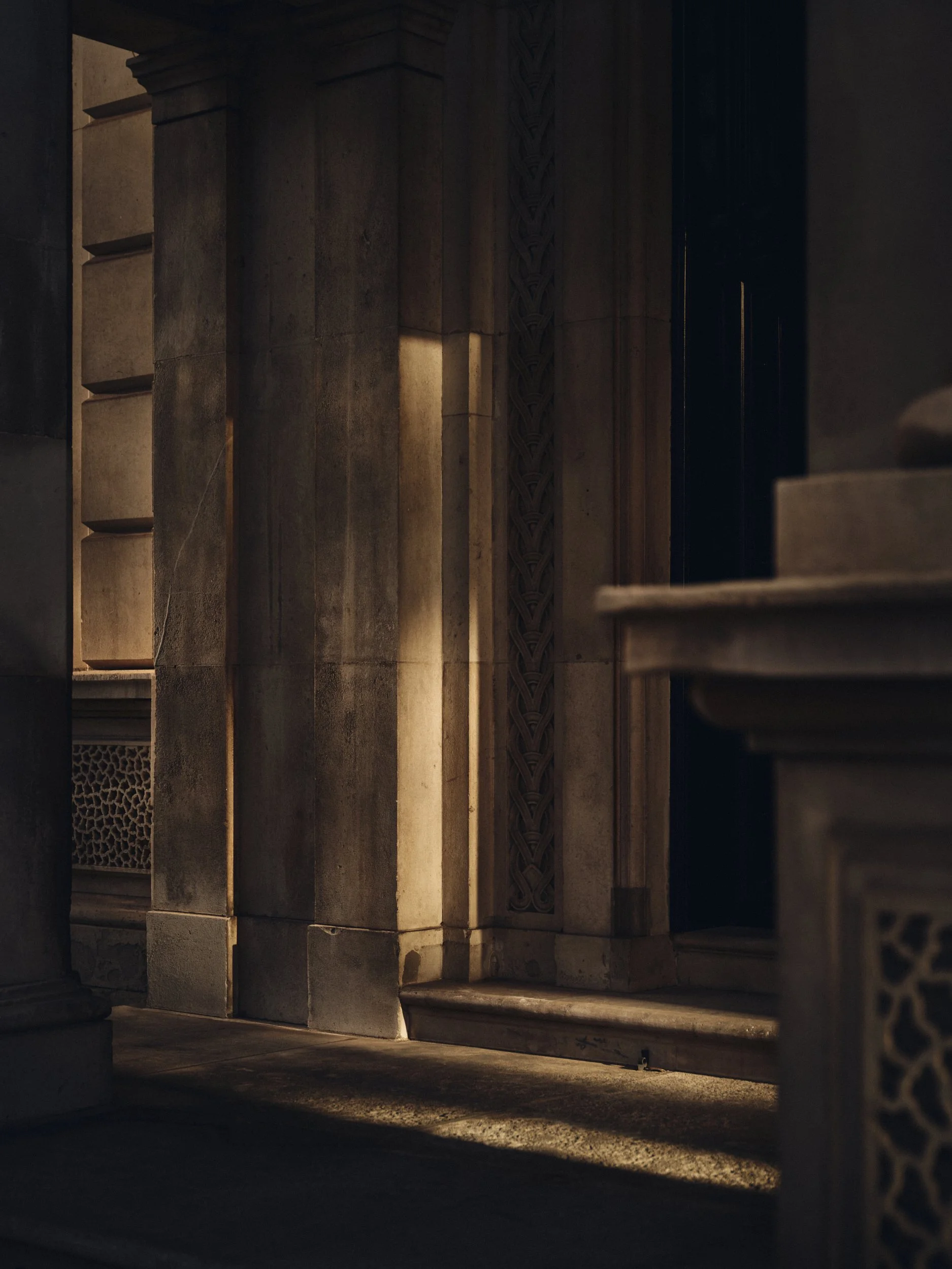 Sunlight illuminates a corridor with stone walls, arches, and decorative carvings.