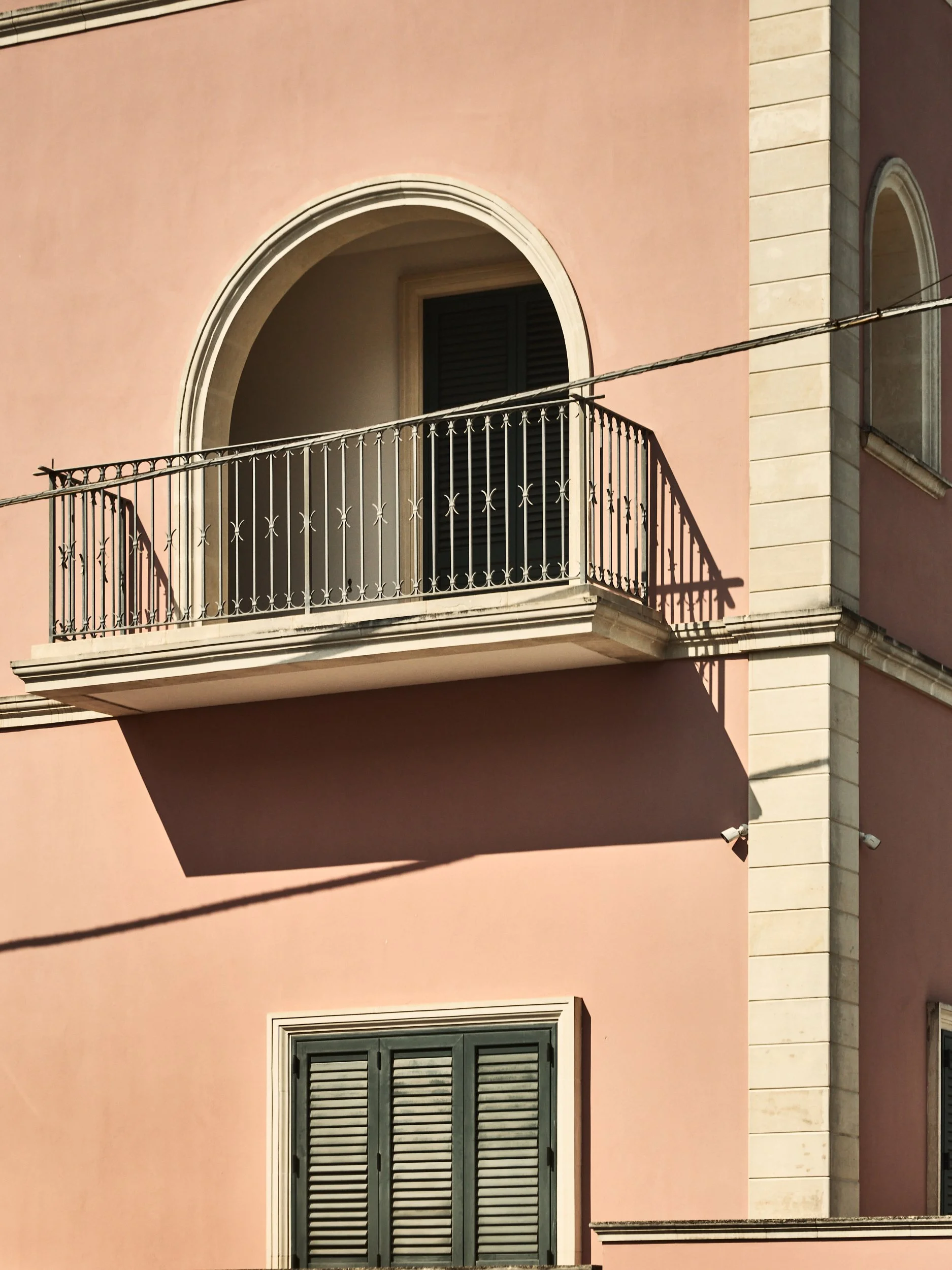 Pink building facade with arched window and decked balcony featuring decorative black metal railing.