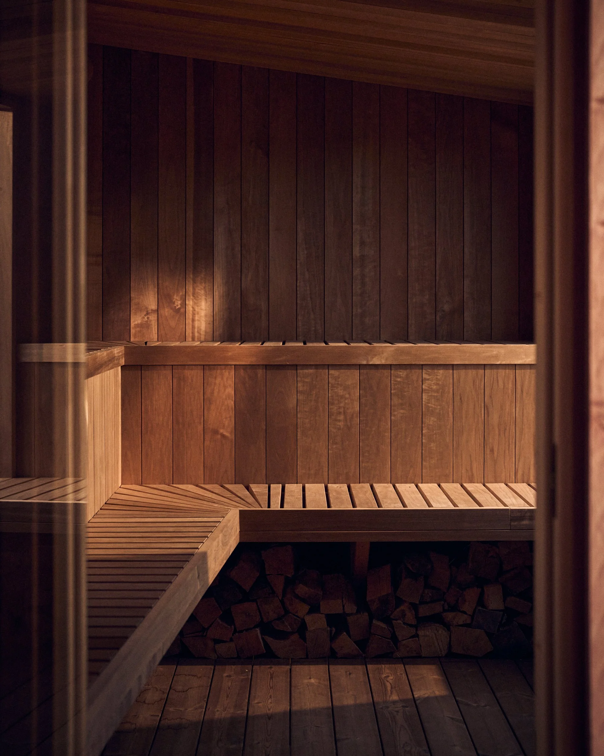 Interior of a wooden sauna with wood paneling on the walls and logs stored in a corner.