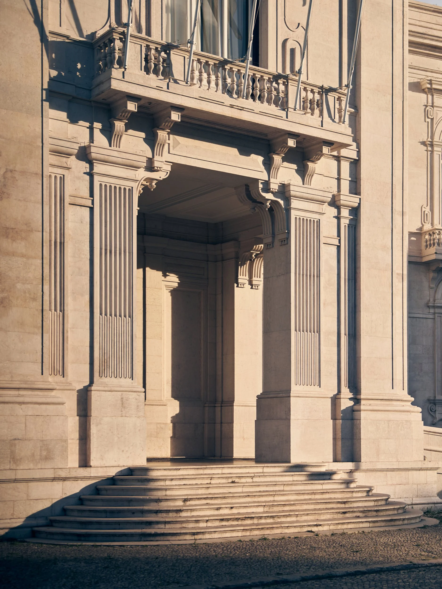 Close-up of classical architectural building facade with columns, a balcony, and decorative stone details.