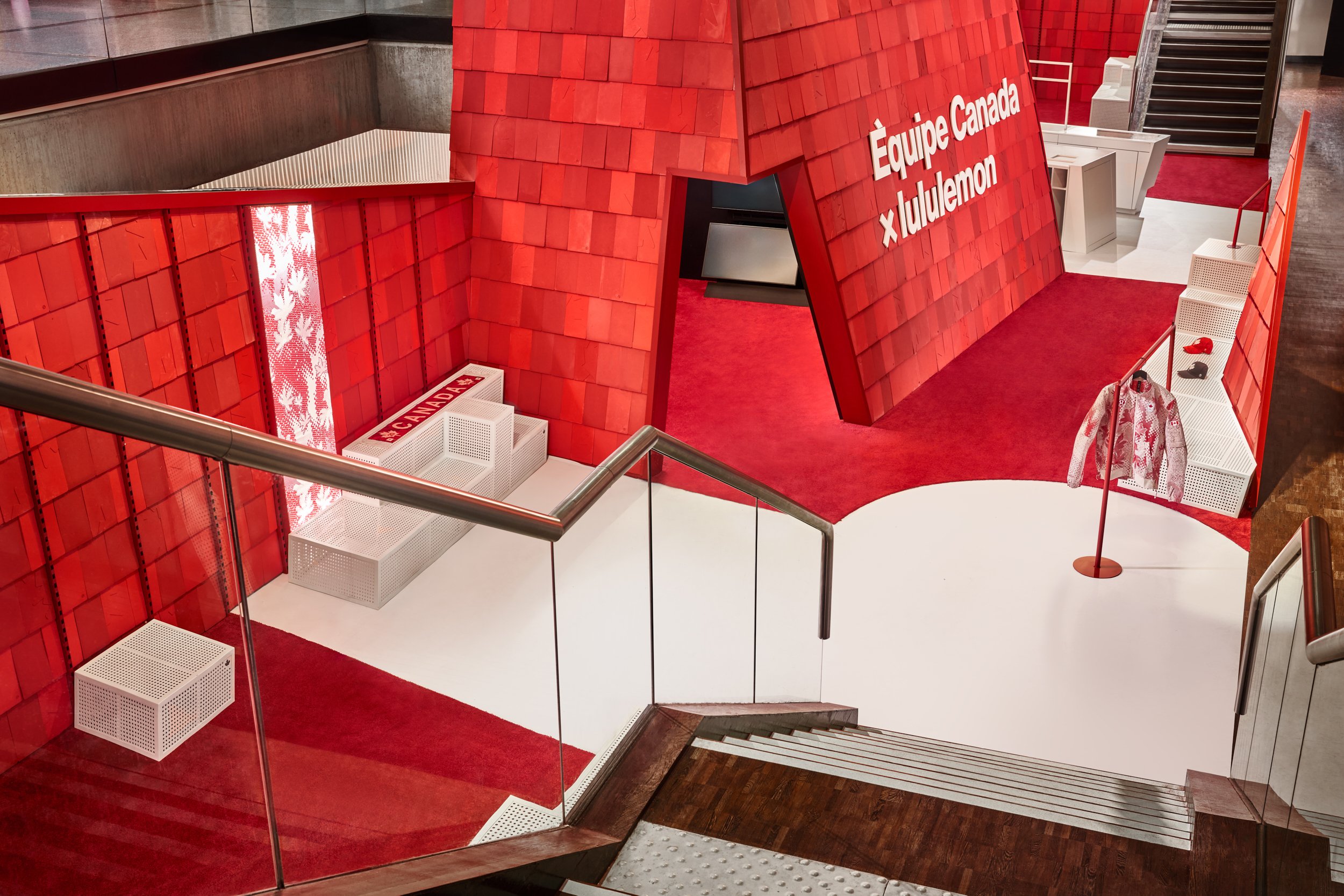 Indoor display with red walls and signage for Équipe Canada x lululemon. The area has white seating and a red carpeted floor.