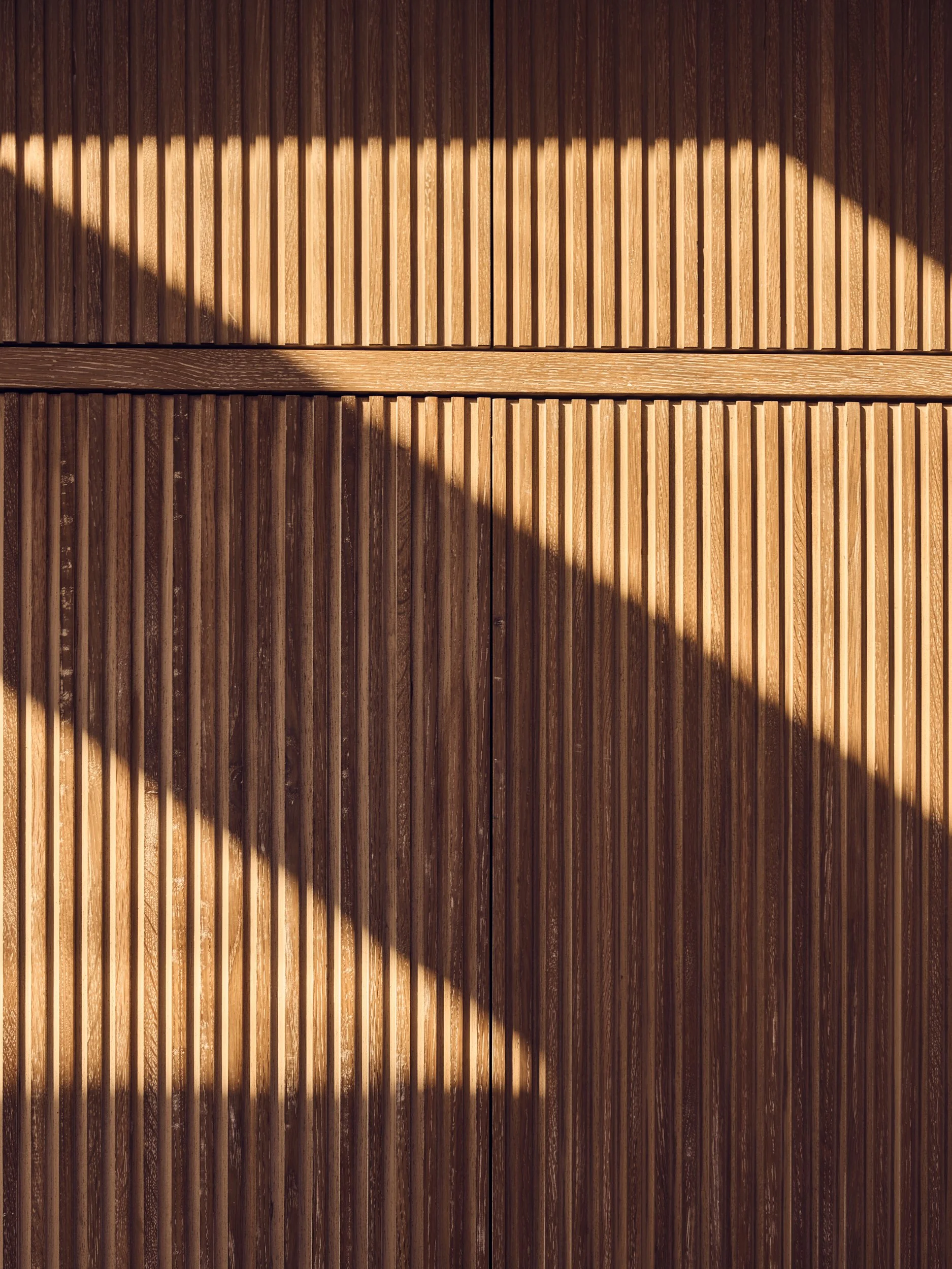 A wooden surface with vertical planks and horizontal beam, partially covered in shadow.