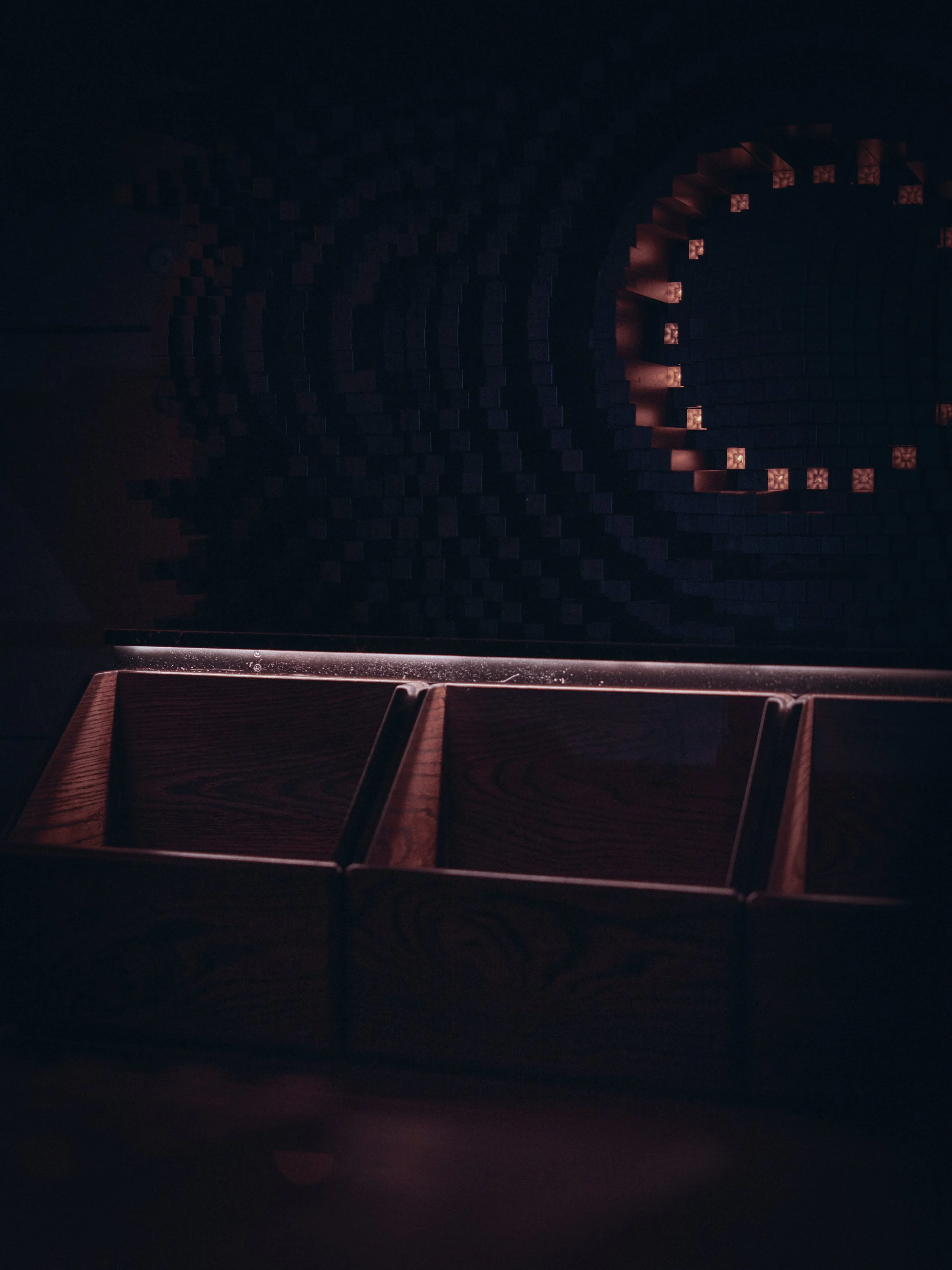 Darkened room with a black wall featuring illuminated red and orange geometric patterns, and a wooden surface with compartments at the bottom.