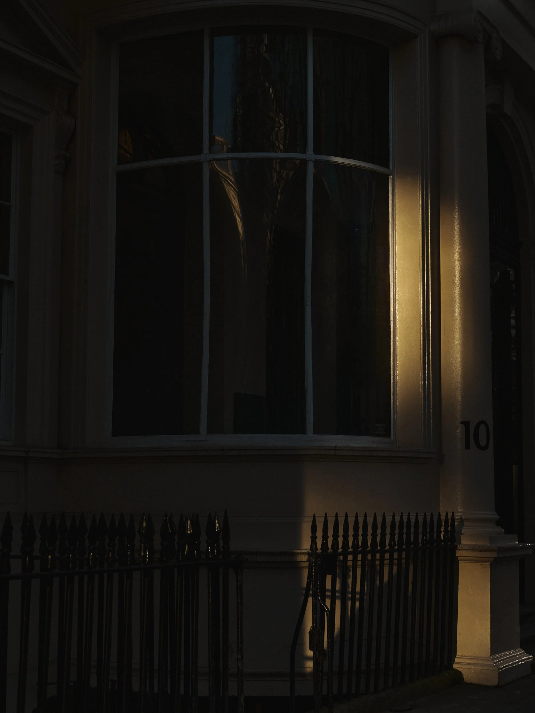 A dark image of a building with a large, arched window and a tall, black wrought iron fence in front.