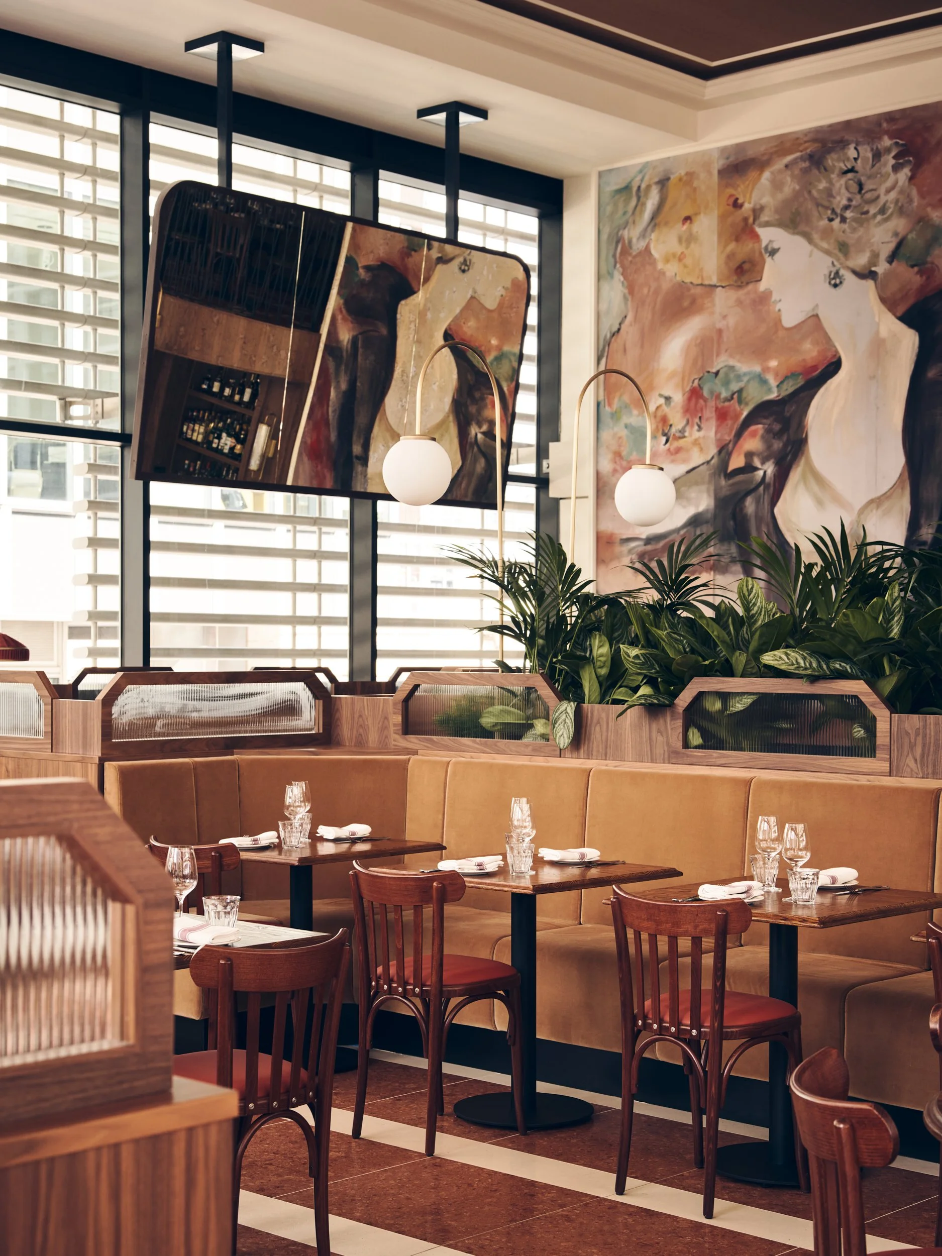 Interior of a restaurant with wooden tables and chairs, large abstract paintings on the walls, and decorative lamps hanging from the ceiling.