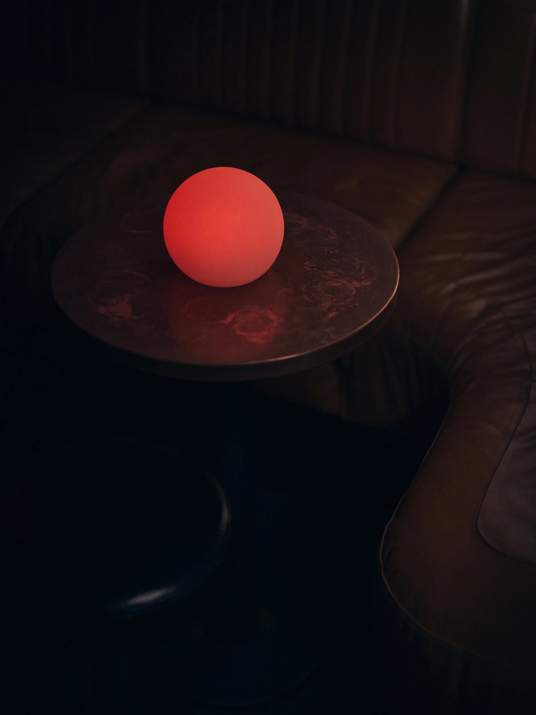 A glowing orange-red spherical object sitting on a dark, reflective surface in a dimly lit room.