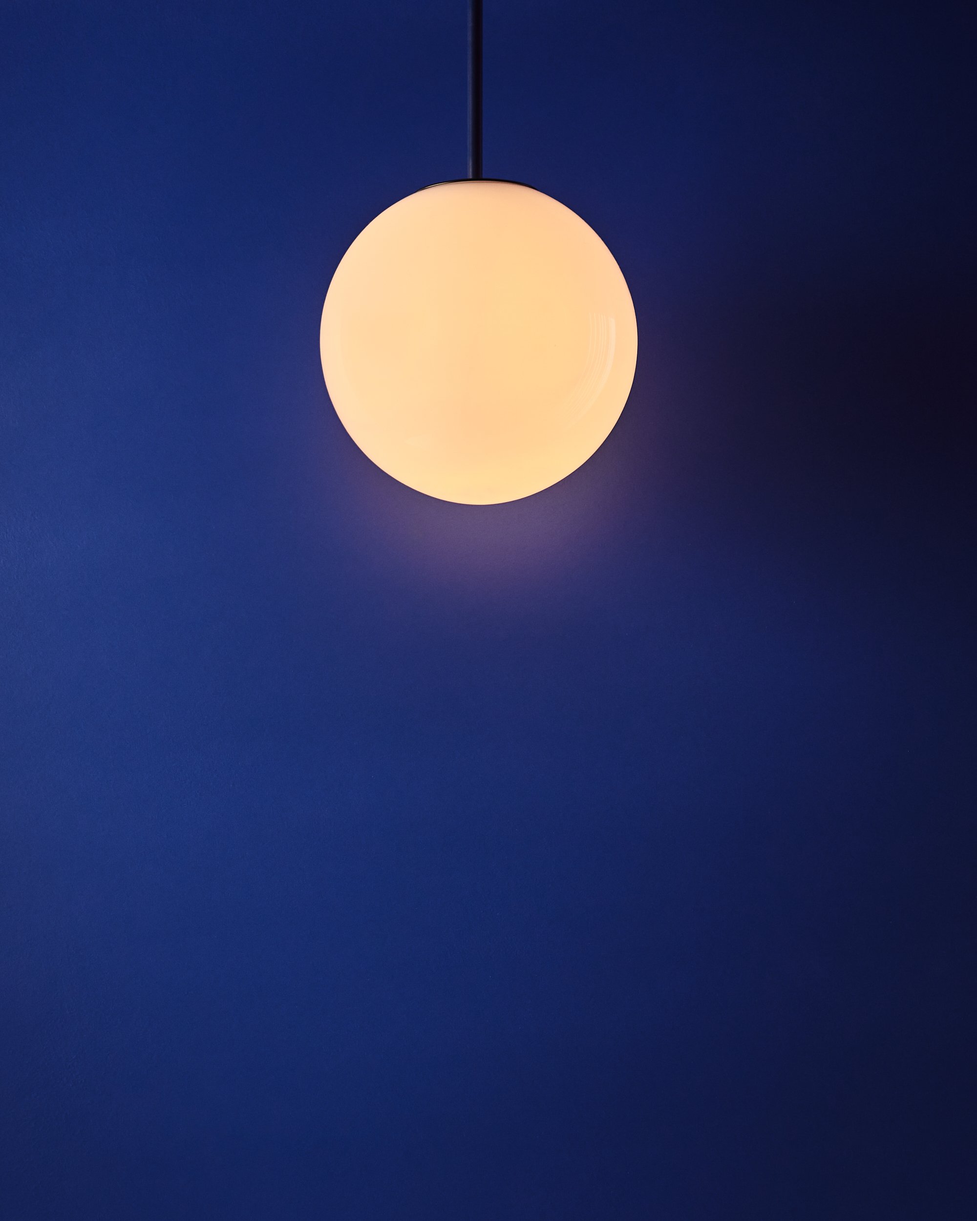 A glowing white spherical pendant light hanging from a black cord against a dark blue wall.