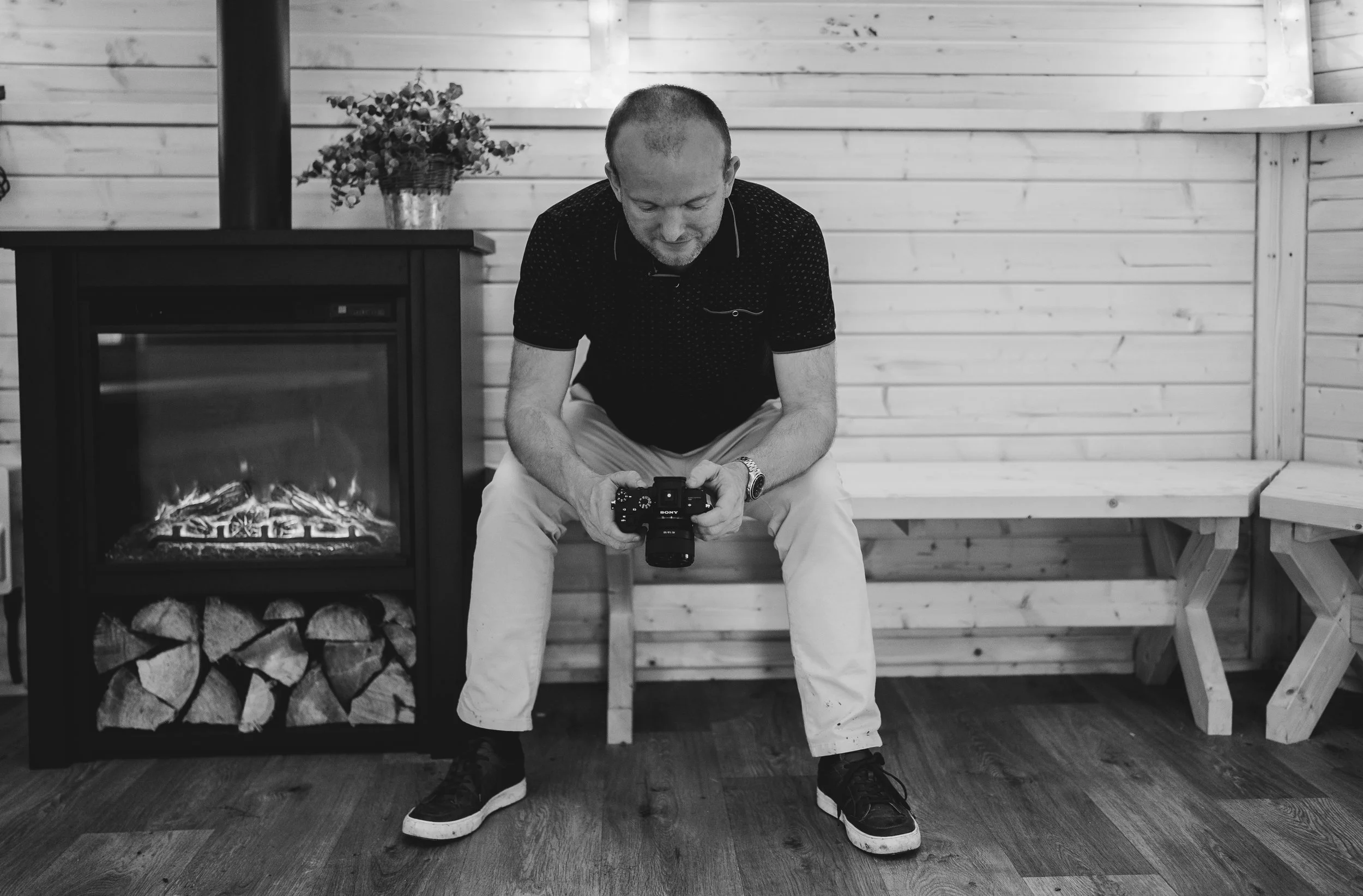 Wedding videographer Terry Anderson sat with his camera by a fireplace, in black and white.