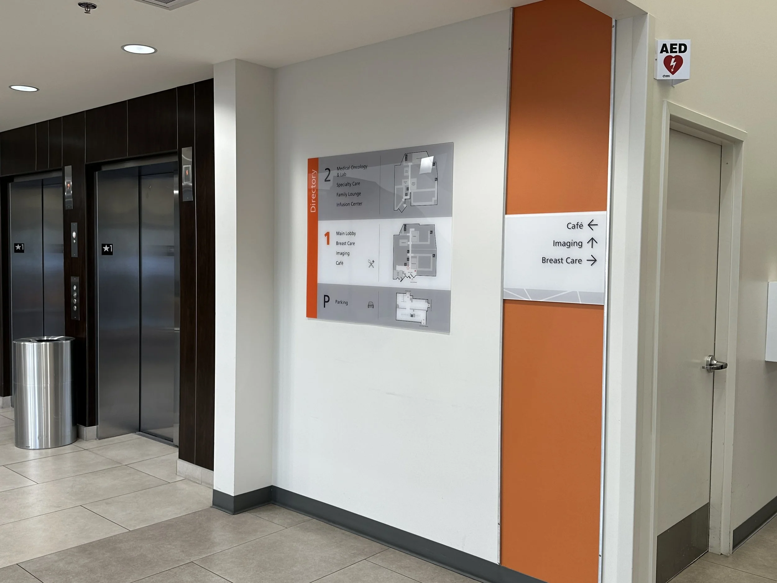 Hospital corridor with directory signs, elevators, and AED device.