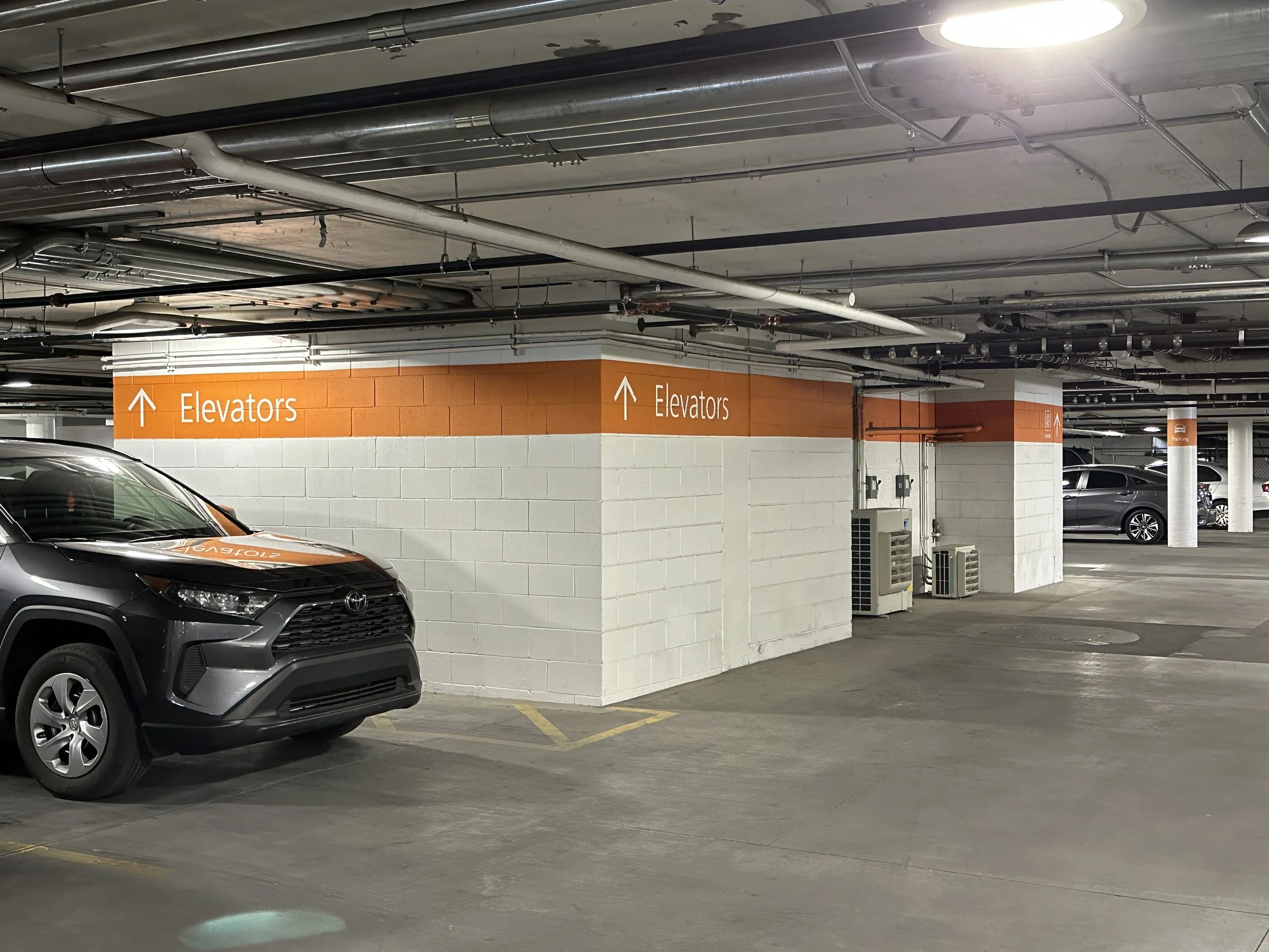 Underground parking garage with directional sign for elevators and parked cars.