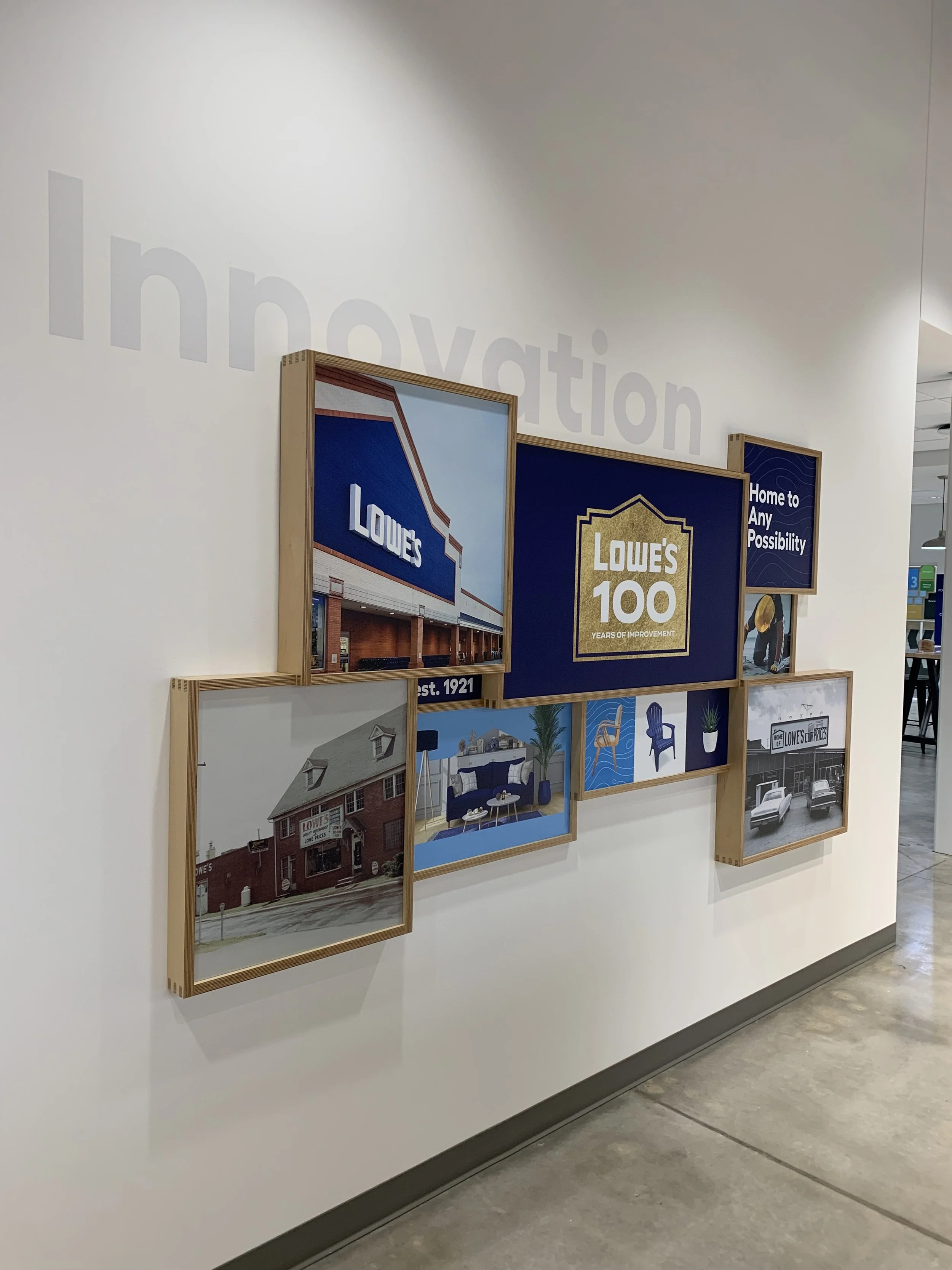 Wall display featuring framed images and graphics celebrating Lowe's history and innovation. Includes a picture of a Lowe's storefront and signs highlighting the company's 100th anniversary.