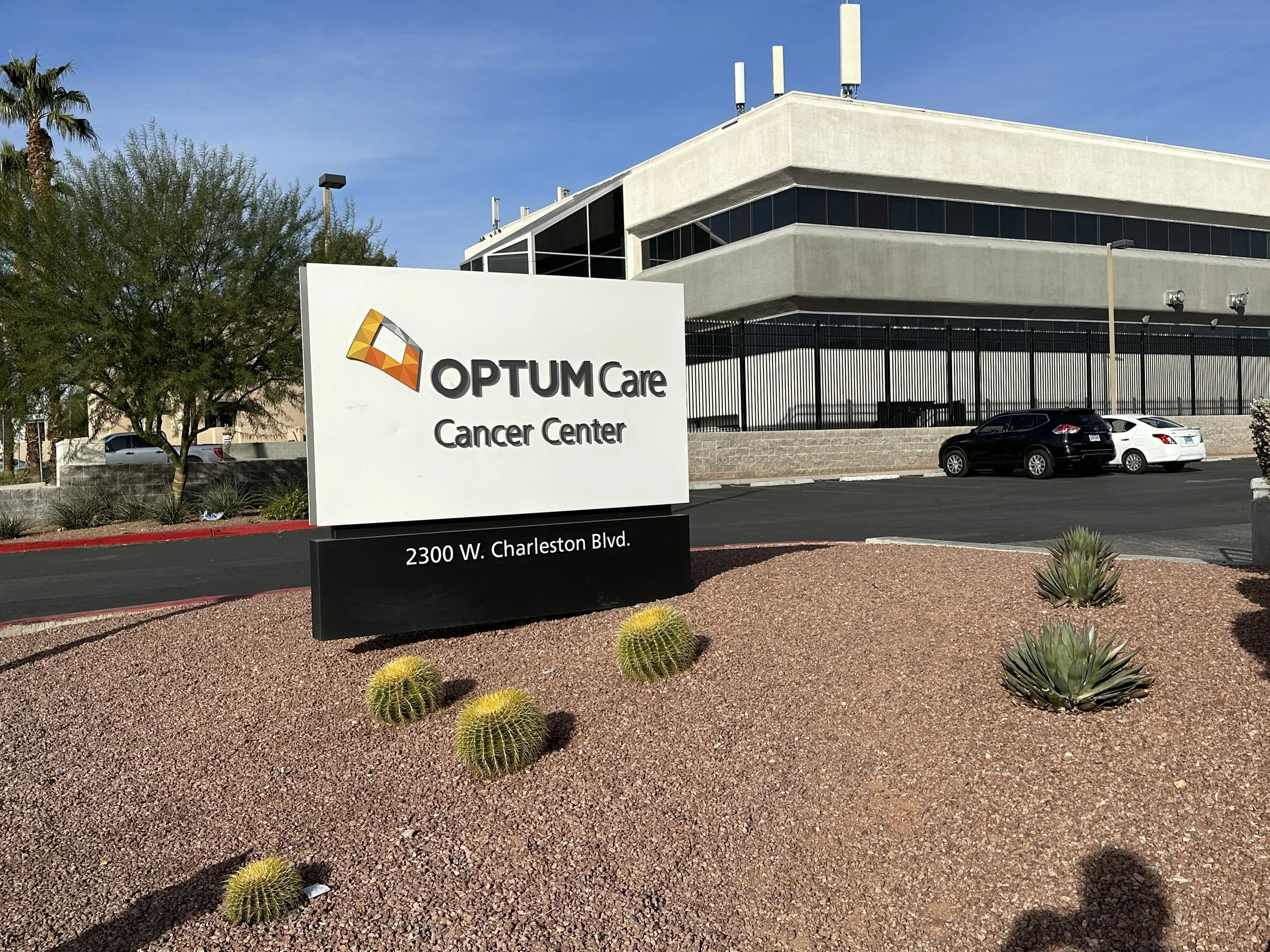 Sign for OptumCare Cancer Center on desert landscape with cacti and parking lot in the background.