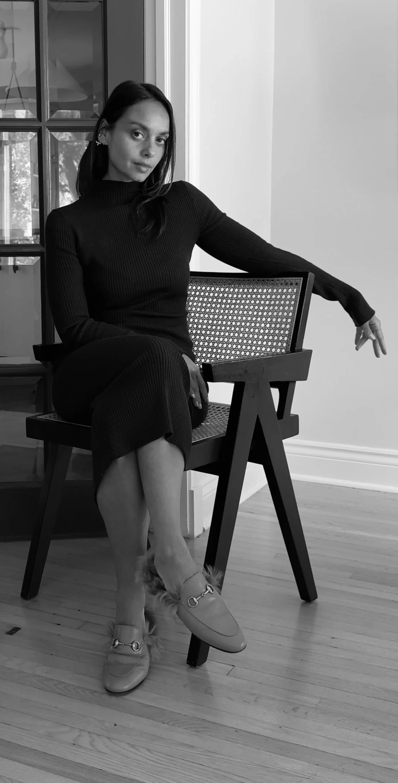 Black and white photo of a woman with shoulder-length dark hair wearing a thick knit sweater, looking to her left with a neutral expression.
