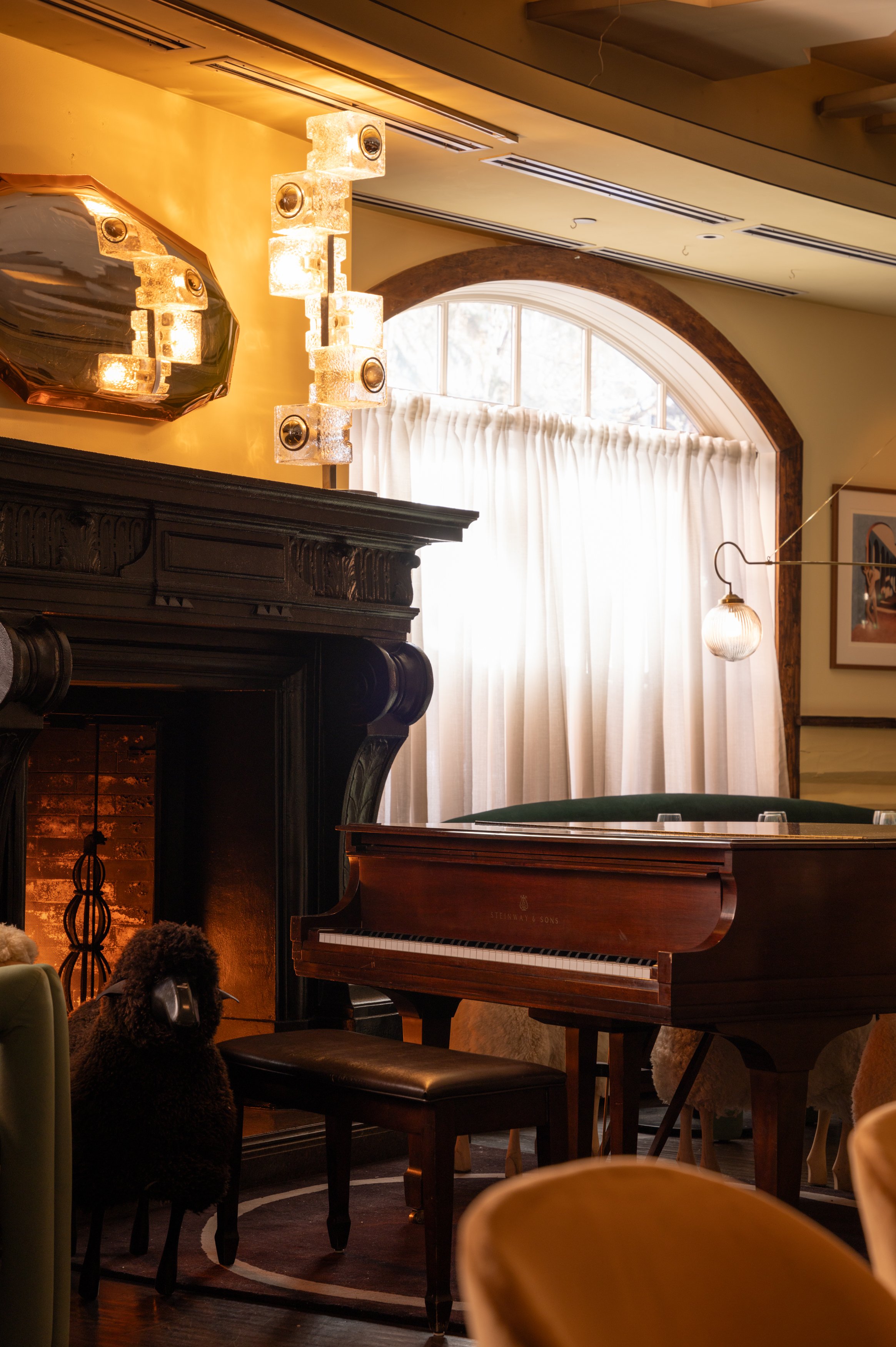 A grand piano beside the fireplace and arched window inside The Snow Lodge