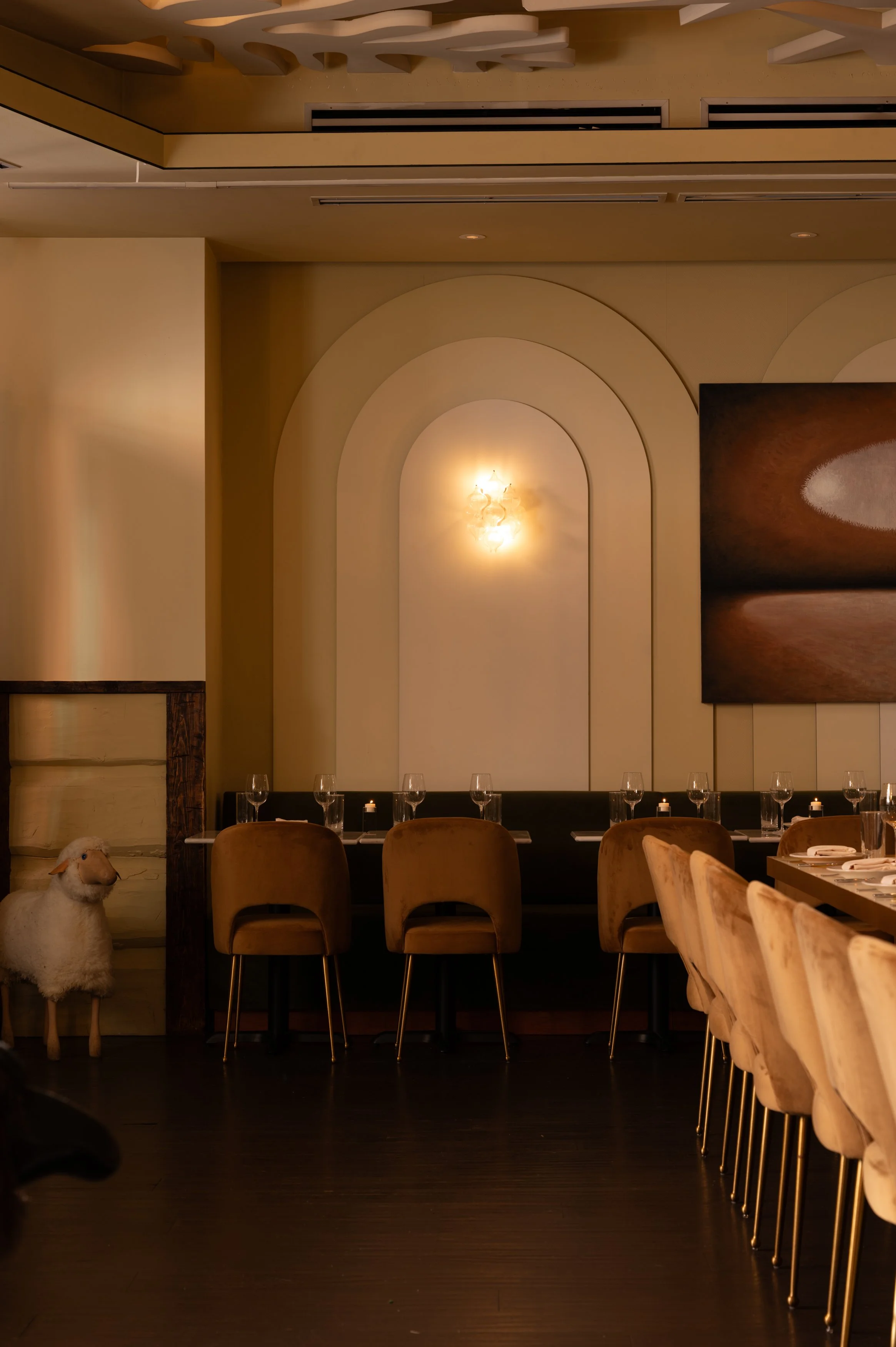 An intimate dining alcove with candlelit tables, artwork, and a decorative sheep figure