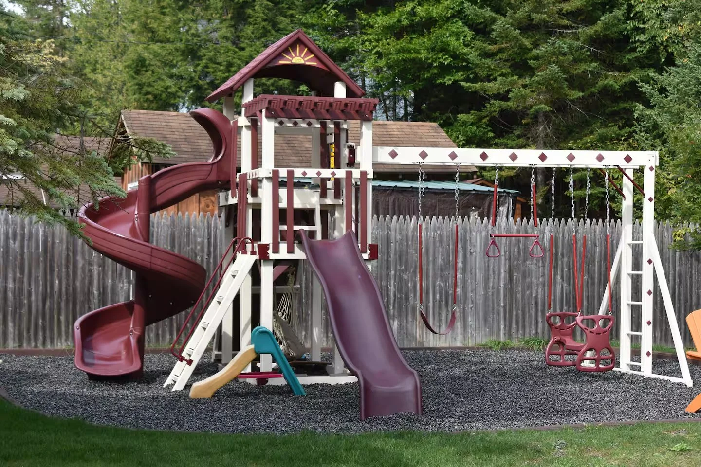 Children's outdoor playset with slides, swings, and climbing features in a backyard.