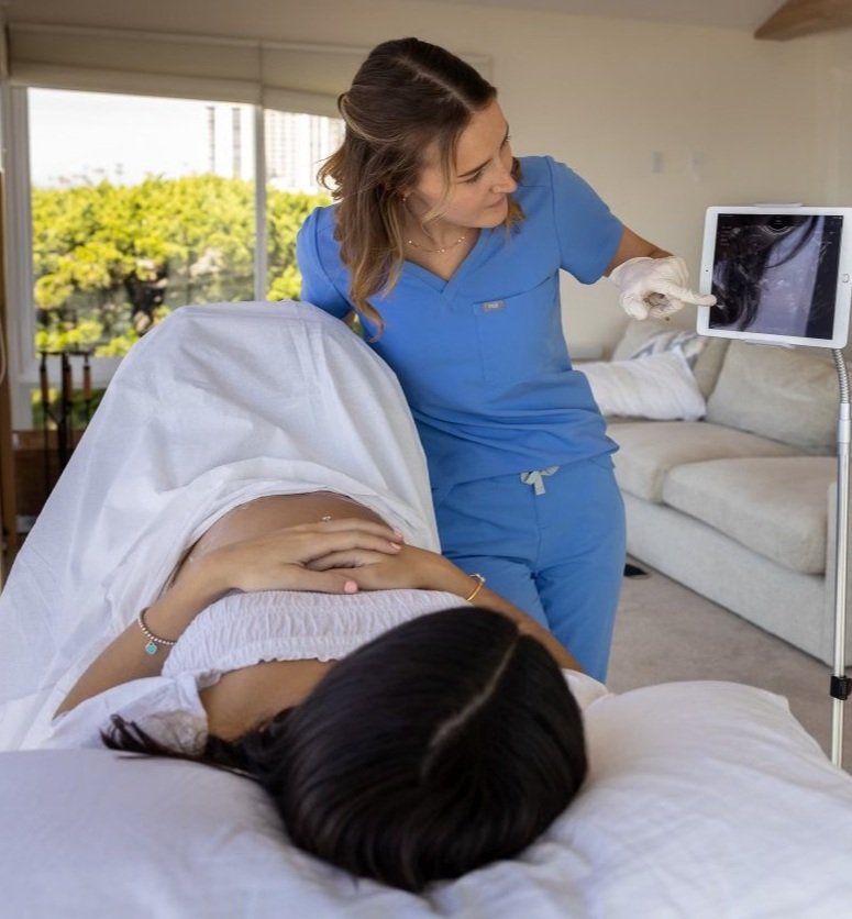 A nurse in blue scrubs showing an ultrasound image to a pregnant woman lying in a hospital bed.