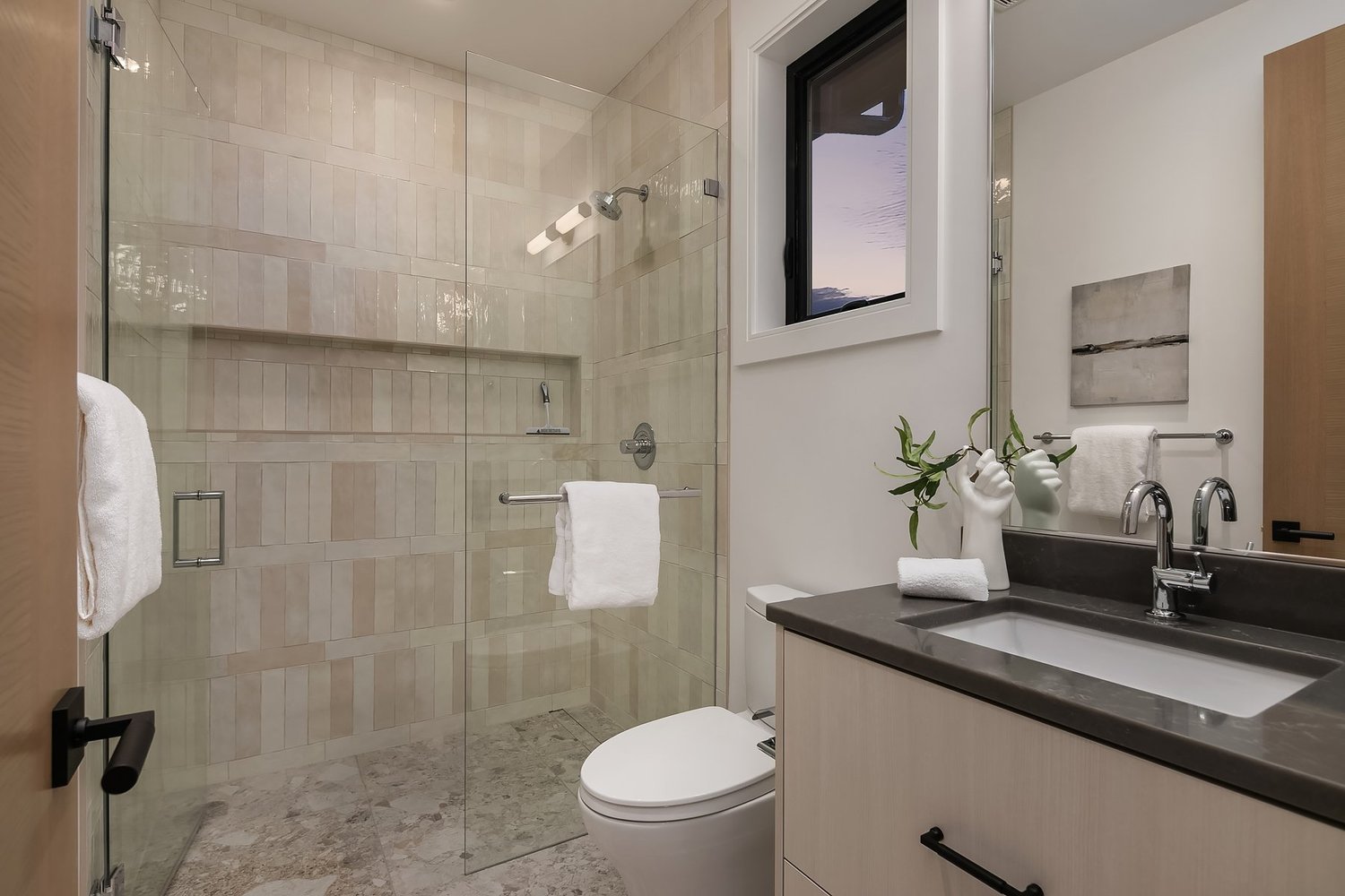 Bathroom with a glass shower, tiled walls, and a dark vanity
