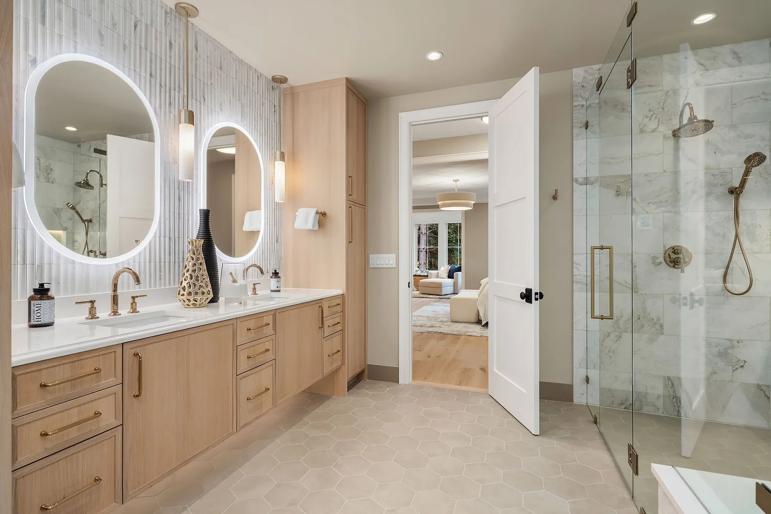 Bathroom with wood vanities, illuminated oval mirrors, and a glass shower